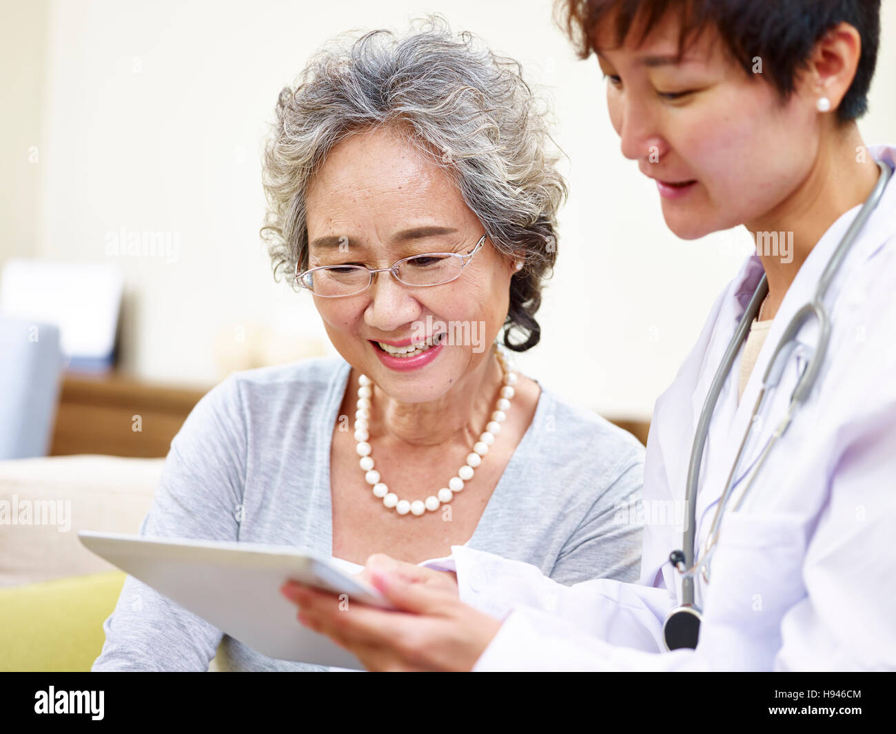 Senior donna asiatica e dal medico di famiglia avente una discussione utilizzando computer tablet Foto Stock