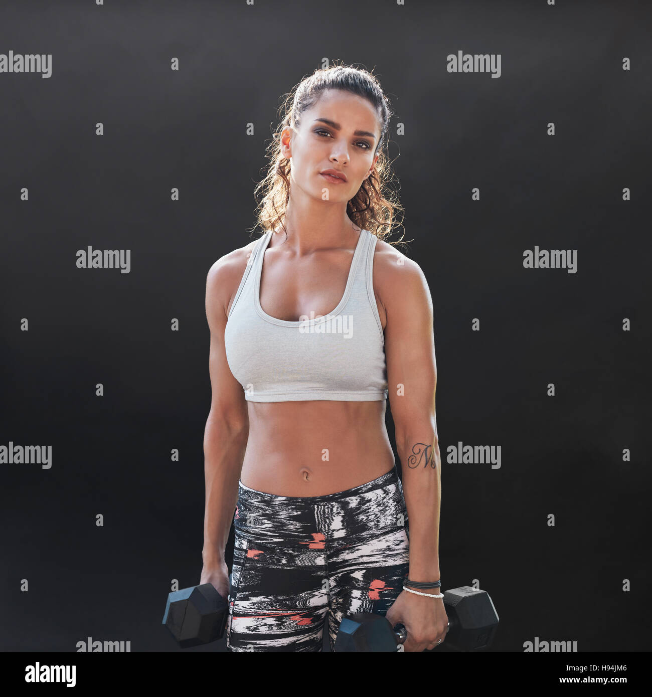 Donna forte e muscolosa che fa allenamento di bodybuilding con i pesi. modello di fitness e bodybuilding. Donna che si allena con manubri sul dorso nero Foto Stock