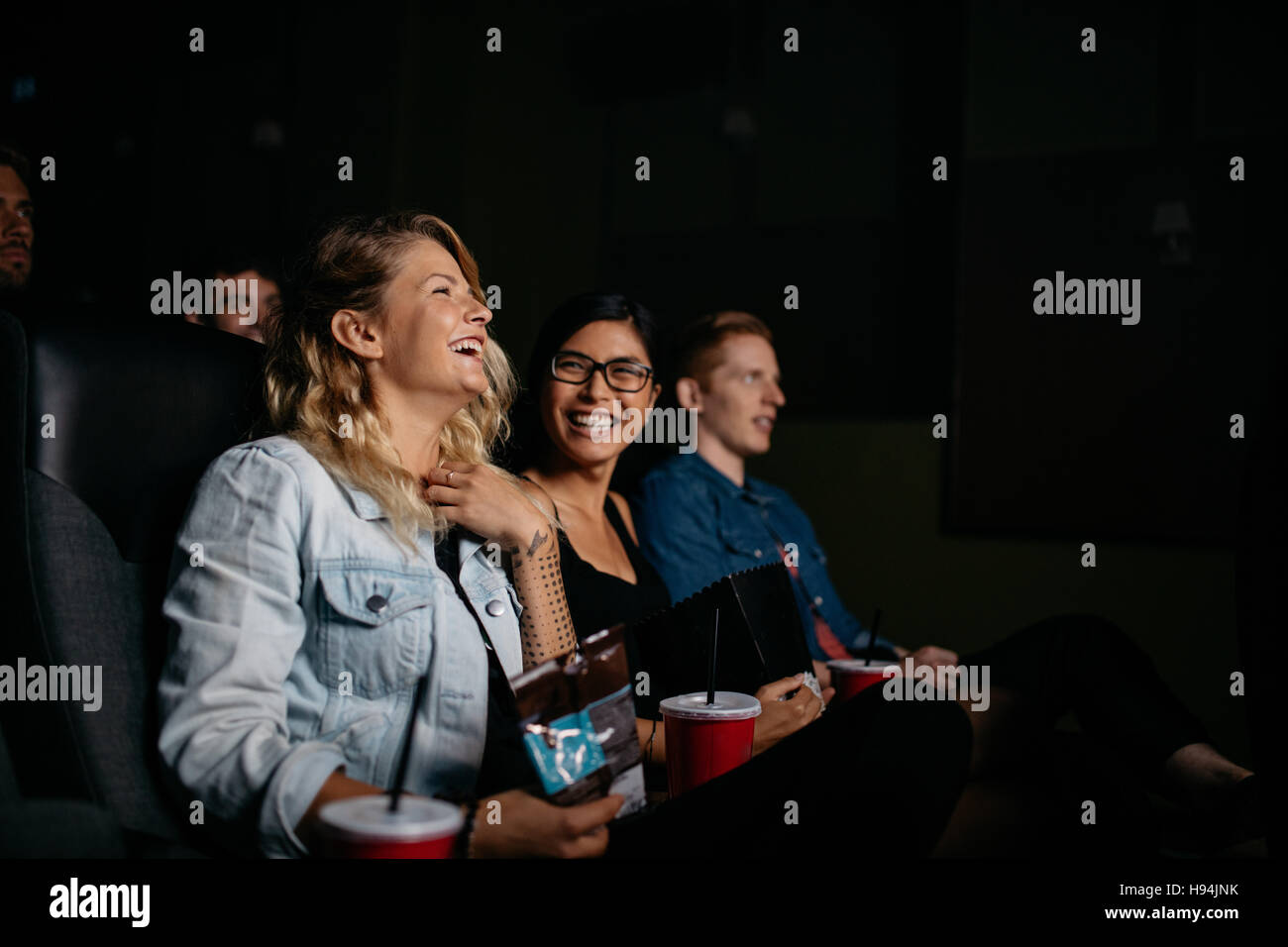 Un gruppo di giovani guardando film per il cinema. Amici seduti nel cinema con popcorn e bevande. Foto Stock