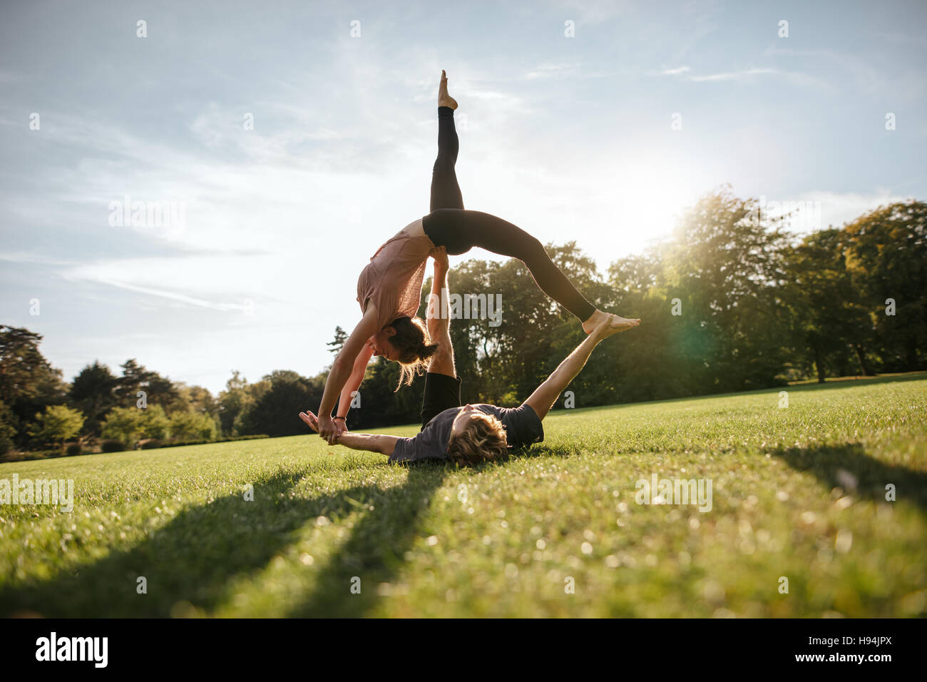 All'aperto colpo di sano giovane uomo disteso su erba e donna di bilanciamento. Montare il giovane facendo acrobatici esercizi di yoga nel parco. Foto Stock