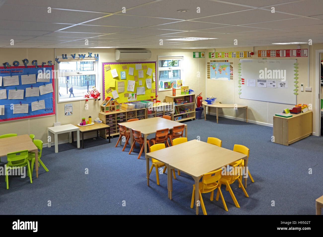 Vivacemente colorato interno di un moderno anno 1 aula scolastica che mostra tavoli sedie ripiani e lavori artistici sulle pareti Foto Stock