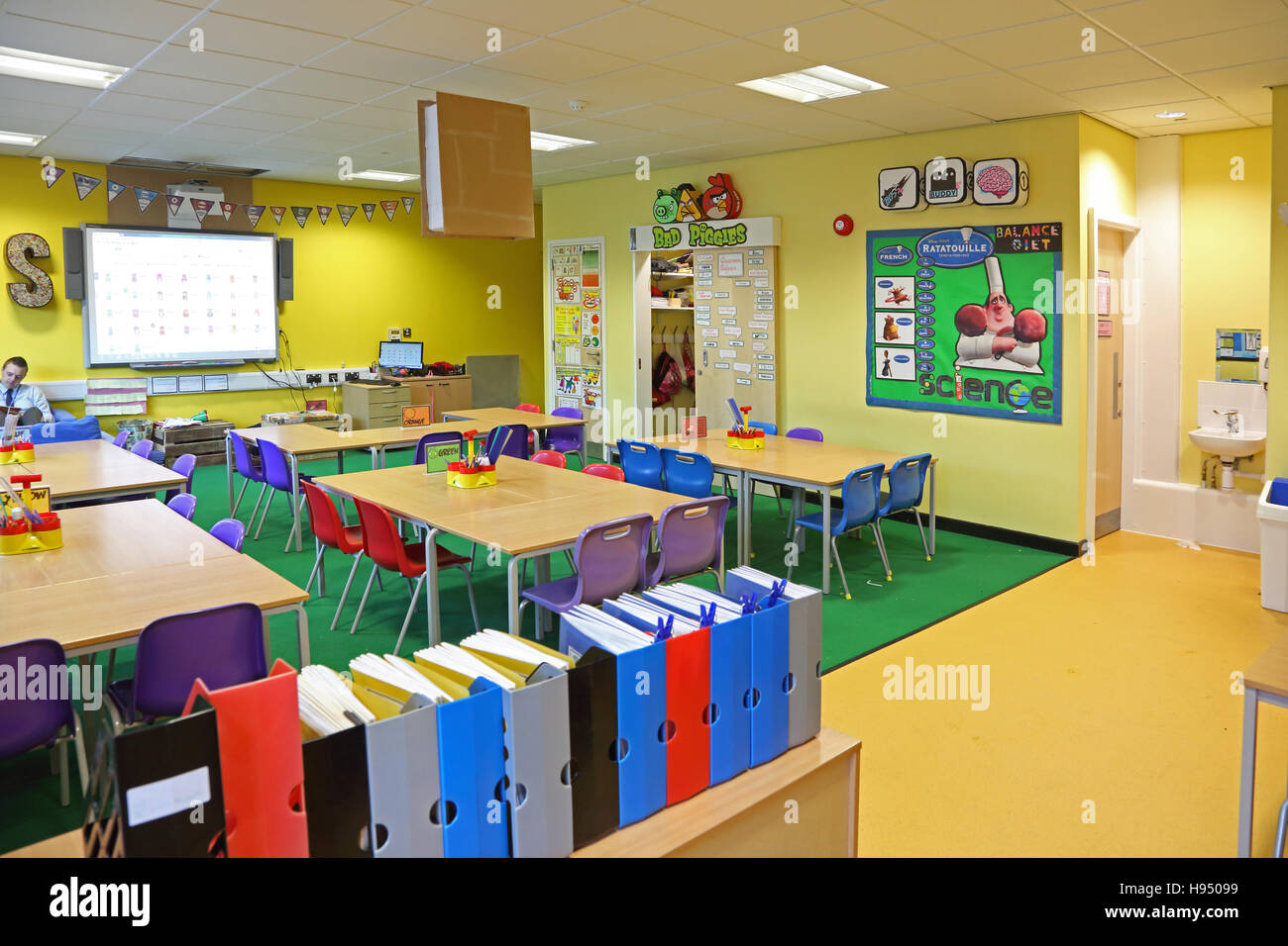 Vivacemente colorato interno di un moderno anno 1 aula scolastica che mostra tavoli, sedie, sullo schermo del computer e lavori artistici sulle pareti Foto Stock