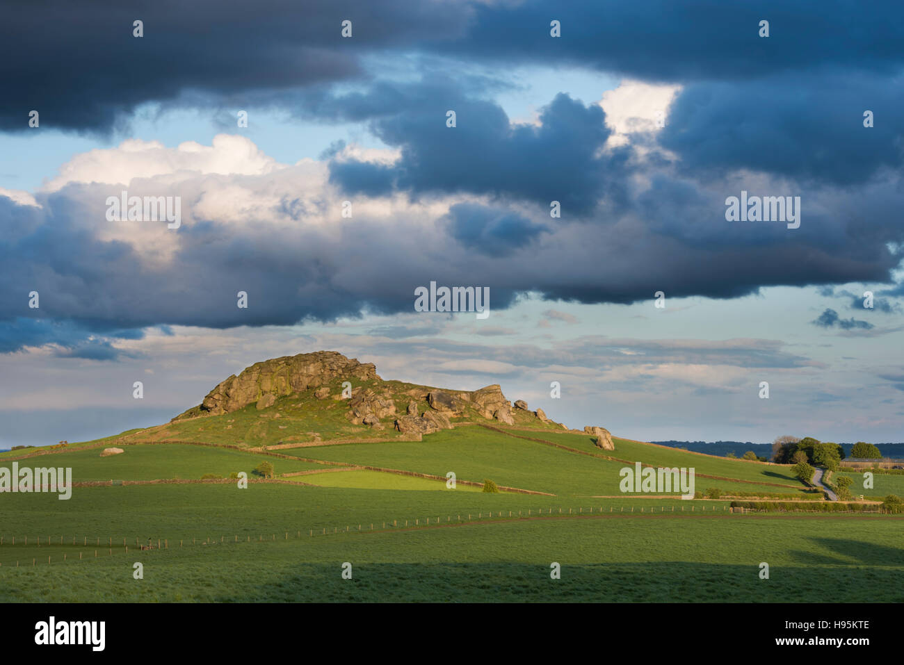 Vista della collina di Almscliffe Crag illuminata dal sole (gritstone tor, campi verdi separati da pareti di pietra, splendido paesaggio collinare) - North Yorkshire, Inghilterra UK. Foto Stock