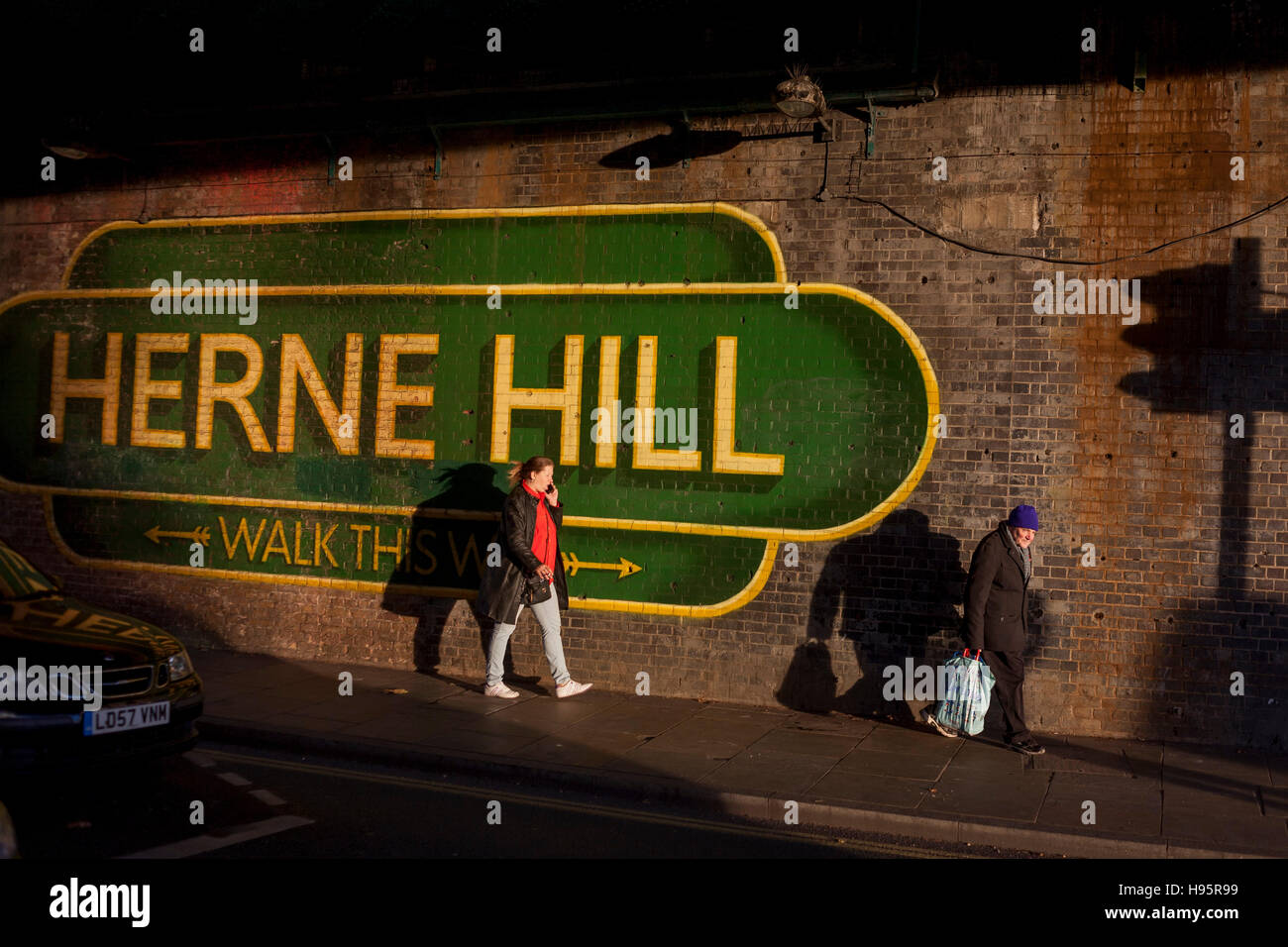 I pedoni a piedi sotto il segno di grandi dimensioni sotto il ponte della ferrovia annunciando Herne Hill, Lambeth SE24 nel sud di Londra. Foto Stock