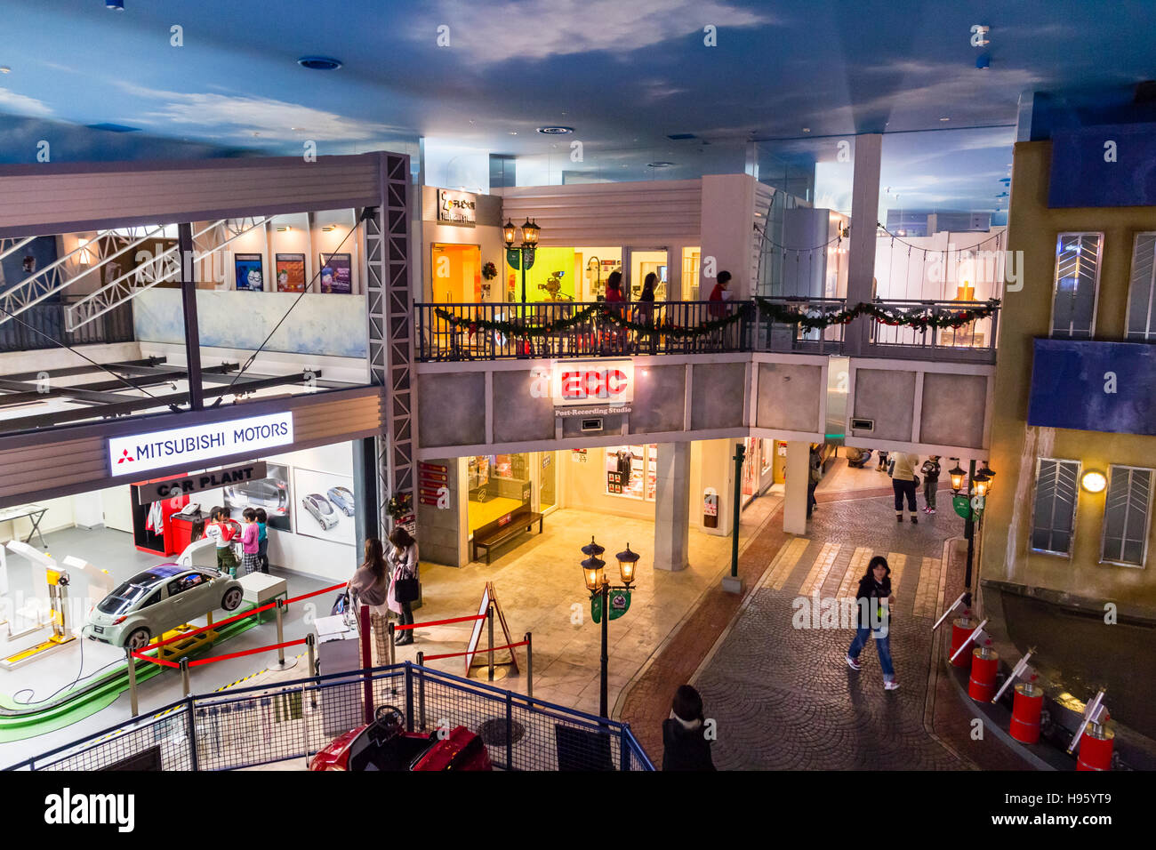 Giappone, Nishinomiya, KidZania, attività per bambini parco giochi. Vista aerea del Mitsubishi Motors garage, edifici e street, alcune persone. Di sera. Foto Stock