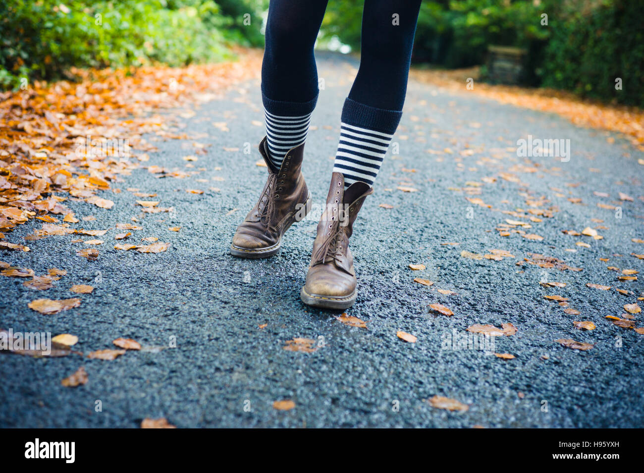 Le gambe di una giovane donna che indossa stripey calzini e scarpe come lei sta camminando su una strada di campagna in autunno Foto Stock