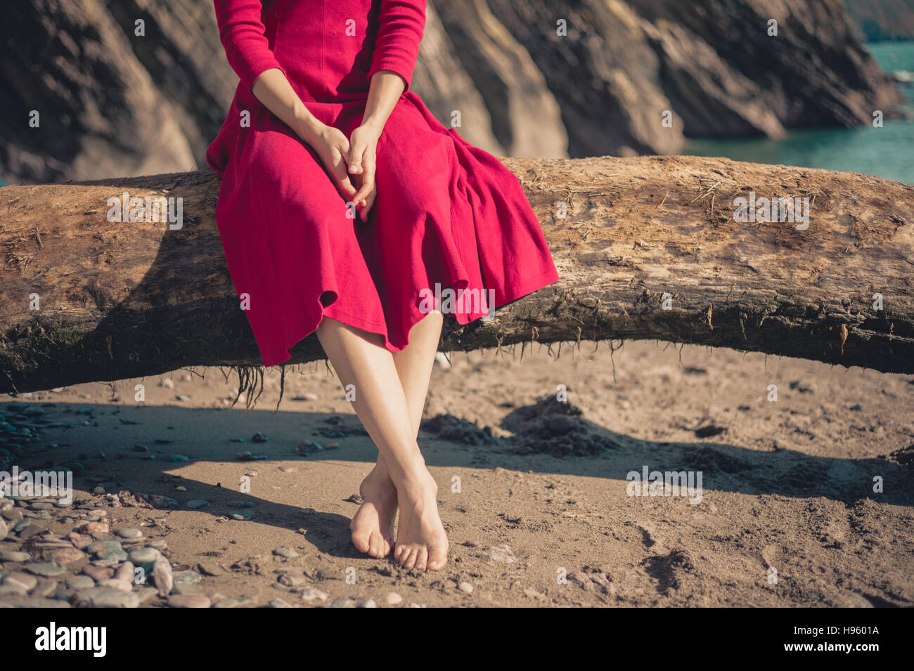 Una giovane donna che indossa un abito rosso è seduto sulla spiaggia e rilassante in una giornata di sole Foto Stock