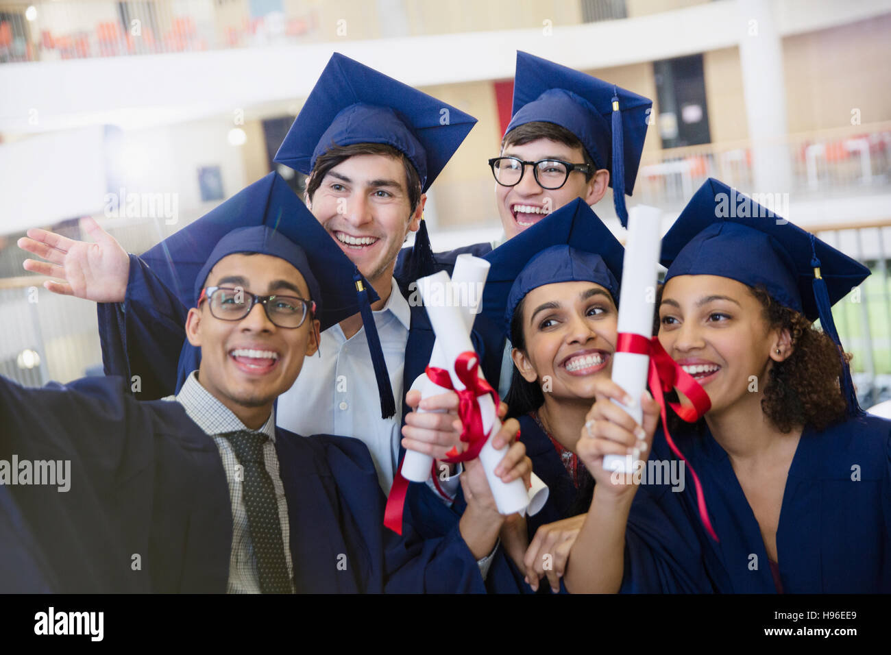 Felice studenti del college nel cappuccio e camice azienda diplomi in posa per selfie Foto Stock