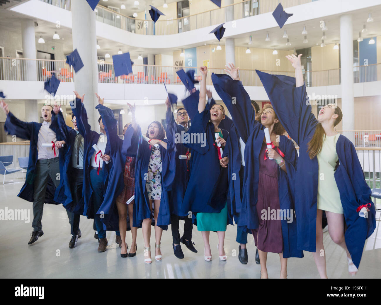 Laureati nel cappuccio e camice gettando overhead di caps Foto Stock