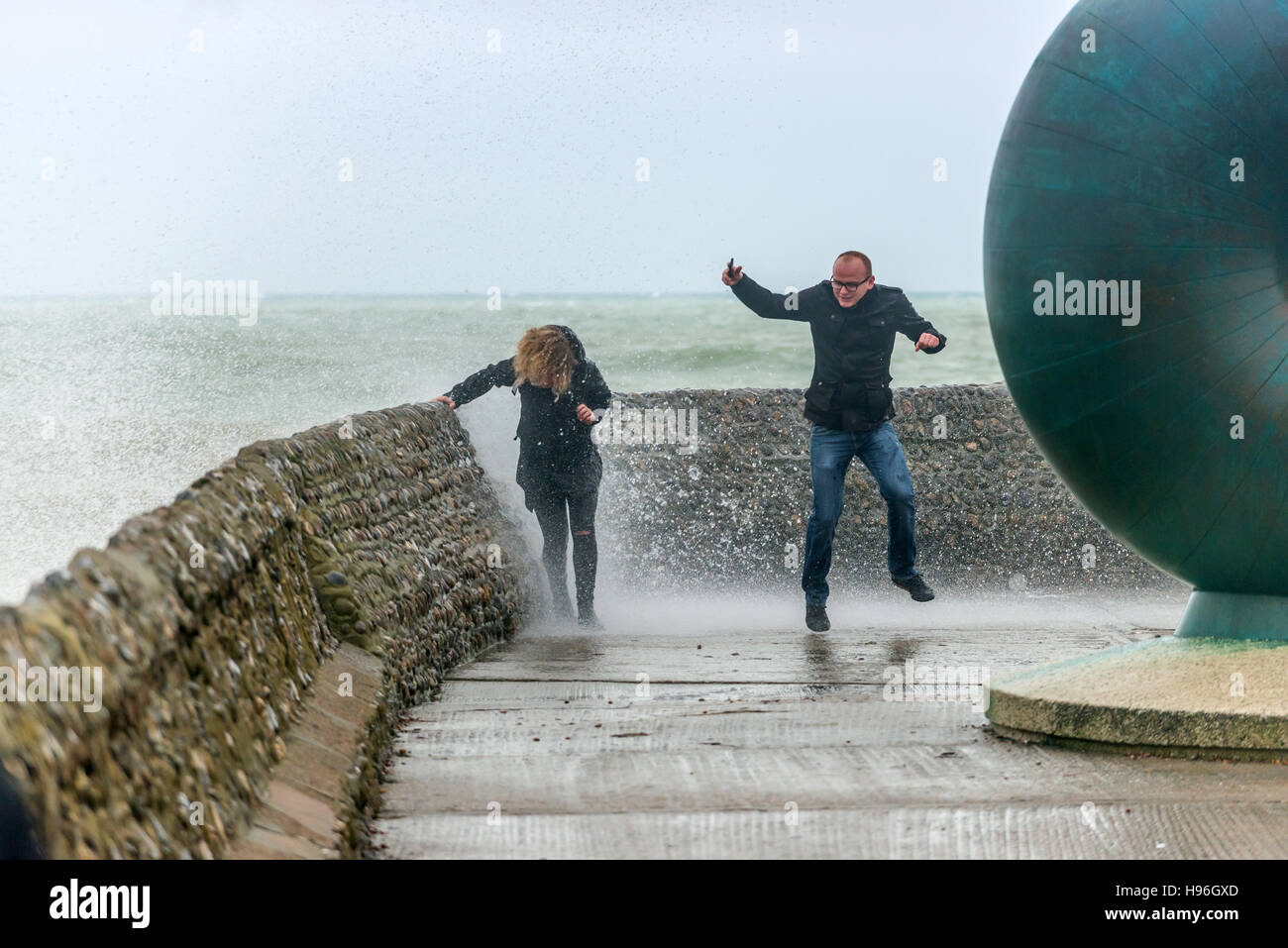 Un giovane cerca di scappare le onde durante una tempesta sul lungomare di Brighton Foto Stock