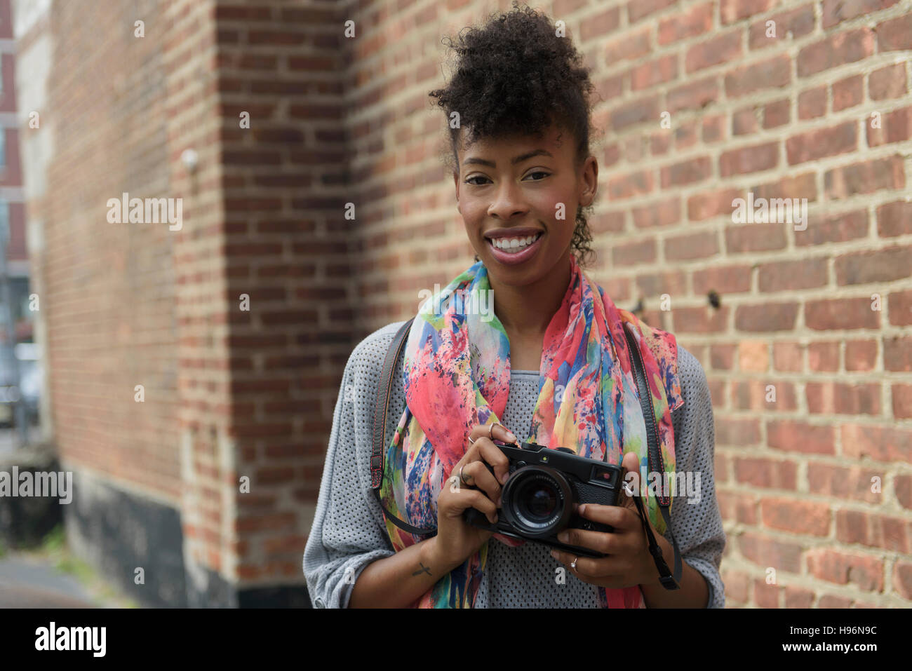 Giovane donna con fotocamera digitale contro un muro di mattoni Foto Stock