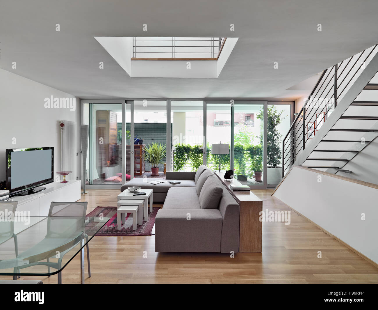Vista interna di un moderno soggiorno con divani di tessuto che si affaccia sulla terrazza e una scala Foto Stock