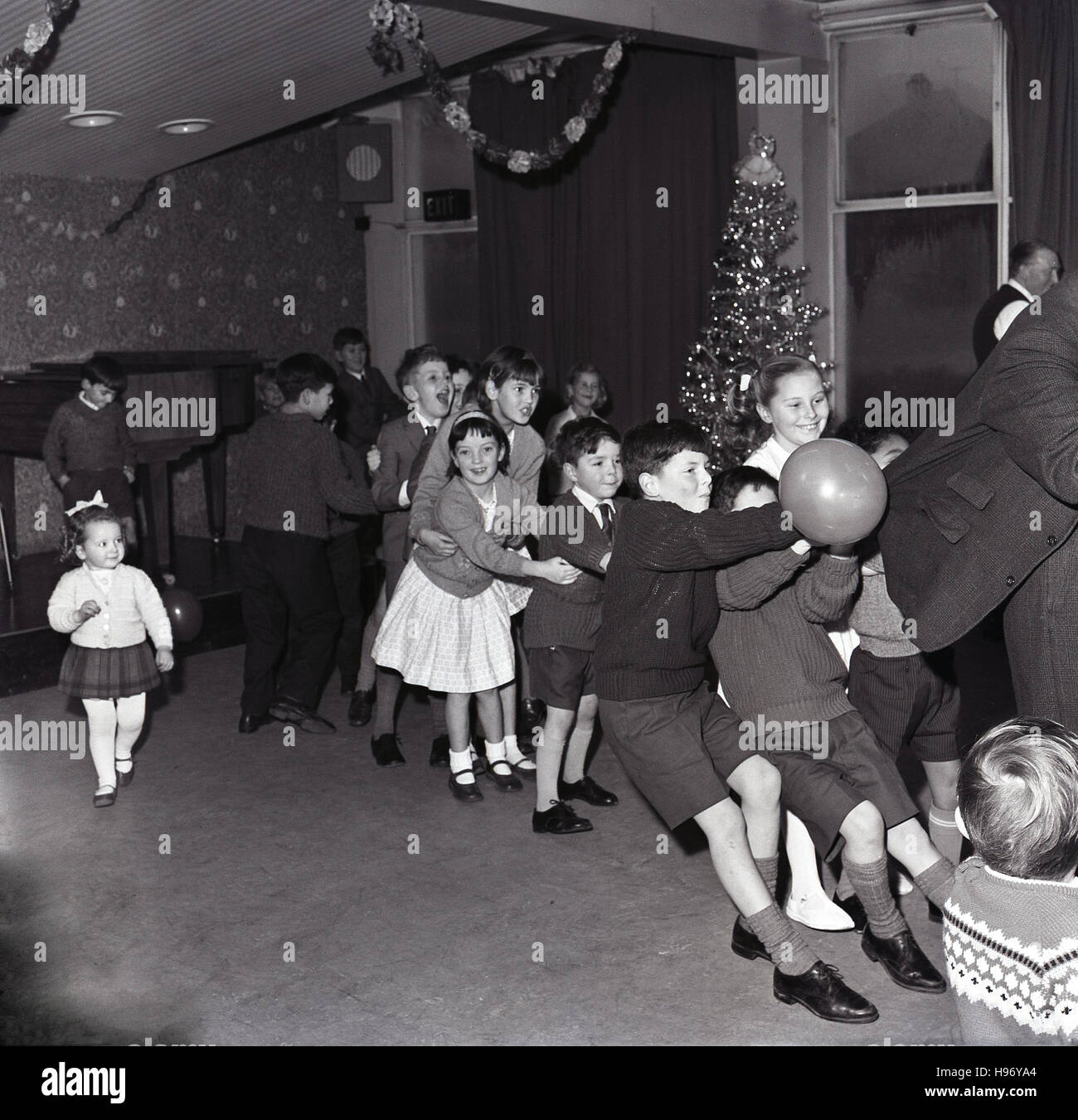 1964, storico, bambini che si divertono ad una festa di natale, una linea dei bambini con i ragazzi presso la tenuta frontale su di un uomo vestito della camicia. Foto Stock