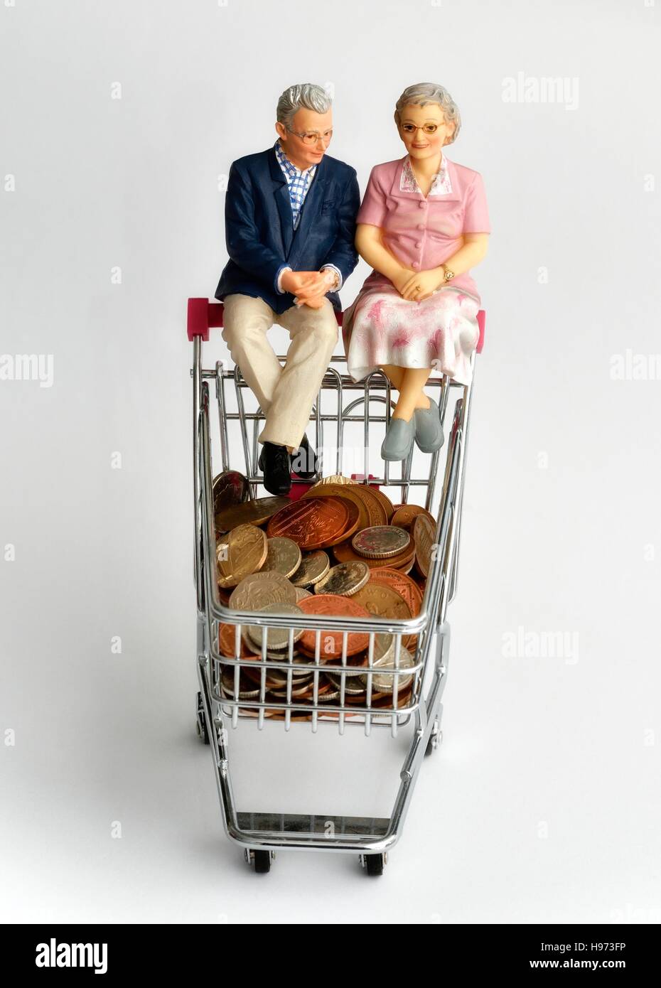 Titolare di una pensione o di una rendita giovane seduto su un carrello della spesa con le monete britanniche all'interno Foto Stock