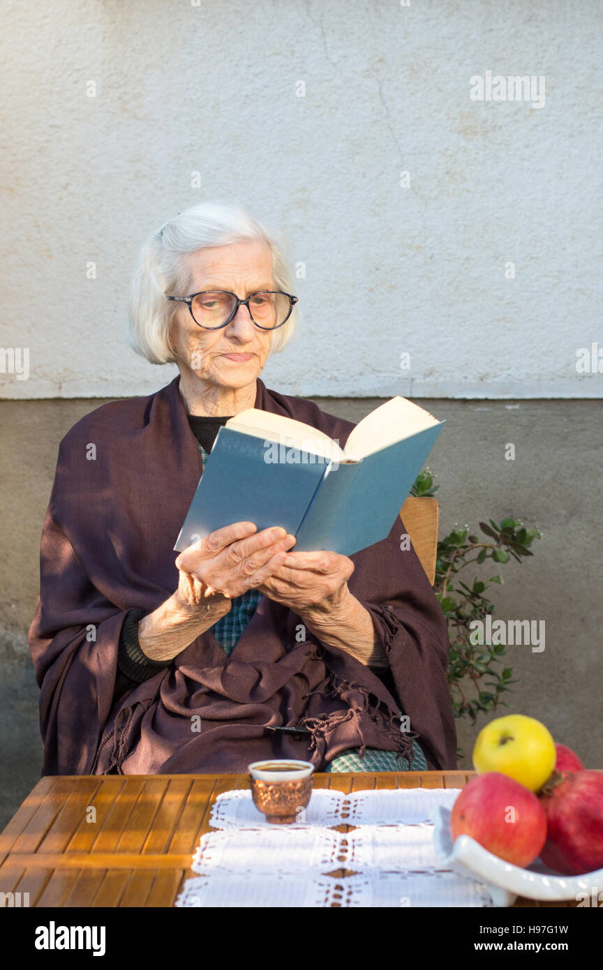 Senior donna la lettura di un libro blu all'aperto Foto Stock