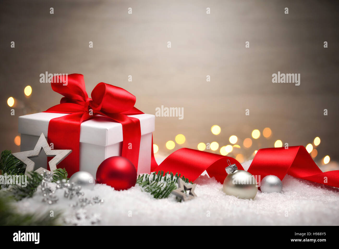 Scena di Natale con una scatola regalo bianca, arco rosso e nastro, luci, baubles, Abete rami e neve, con spazio di copia Foto Stock