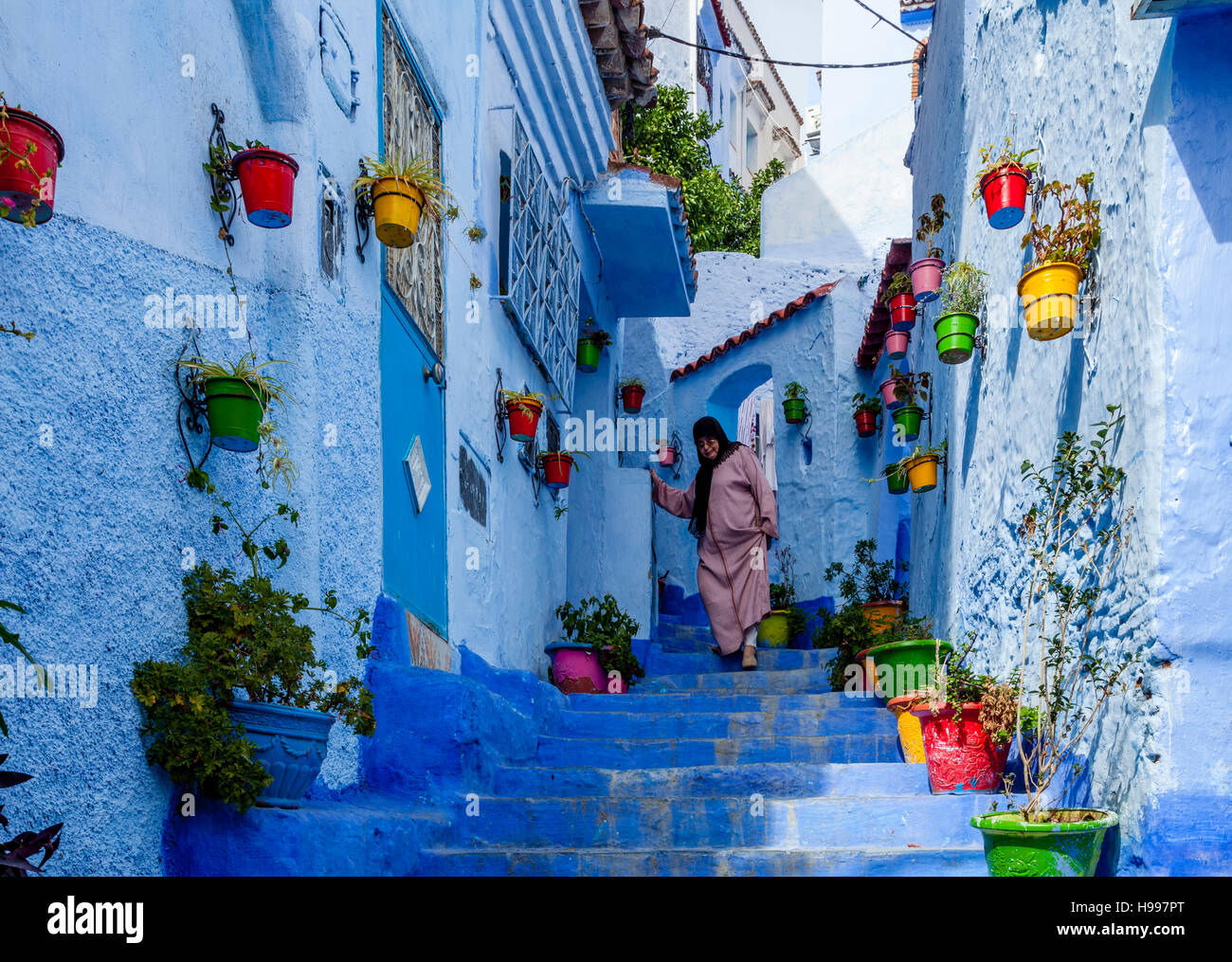 Una donna anziana a piedi giù per una strada colorato nella Medina, Chefchaouen, Marocco Foto Stock