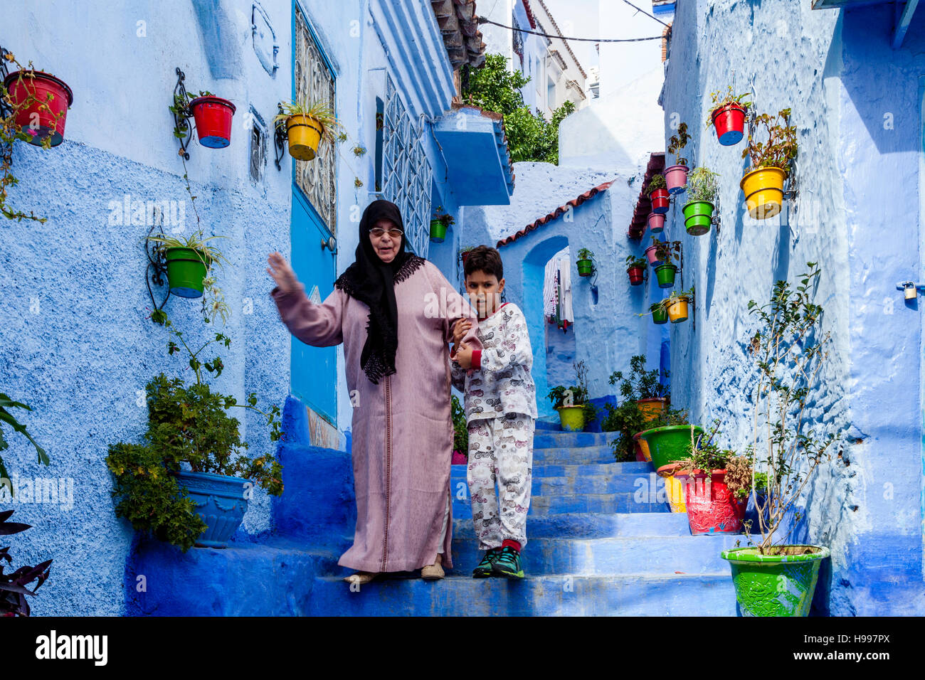 Un giovane ragazzo aiuta una signora anziana giù alcuni passi in una strada nella Medina, Chefchaouen, Marocco Foto Stock