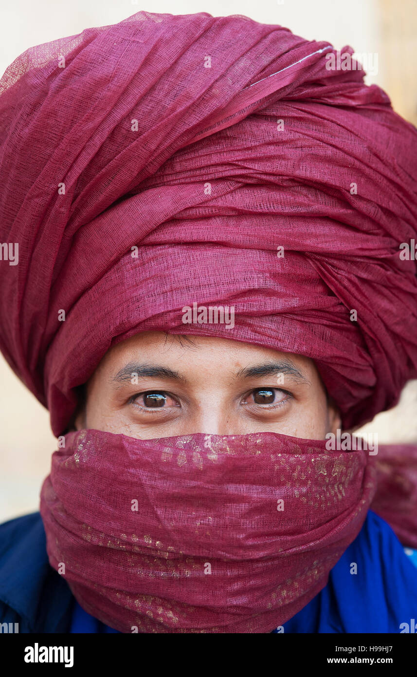 Ritratto di un nomade beduino con turbante rosso scarlatto e fissando gli occhi vende la sua mercanzia in Ait Benhaddou, Marocco. Foto Stock