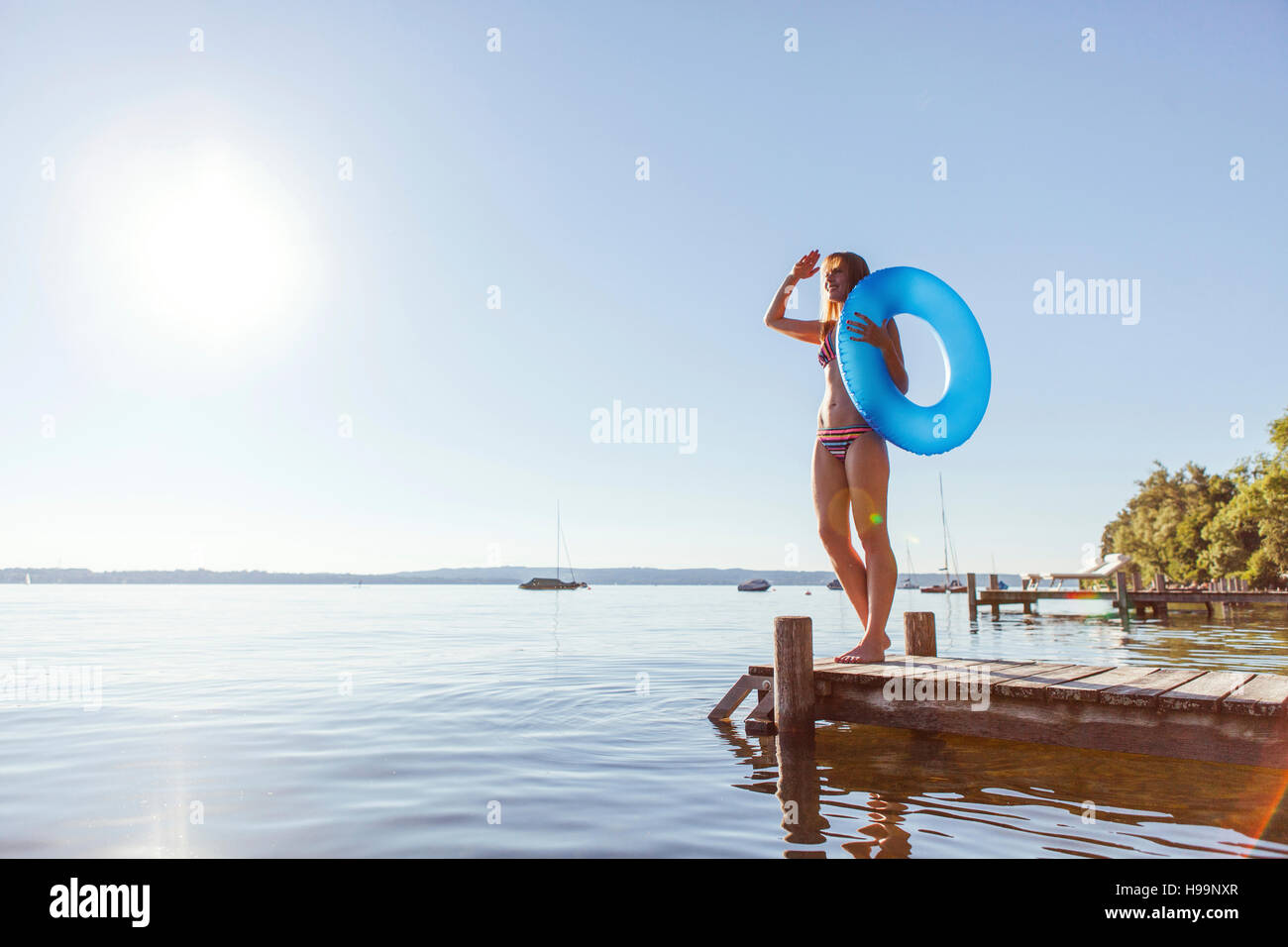 Giovane donna si erge sul molo dal lago di tenuta anello gonfiabile Foto Stock