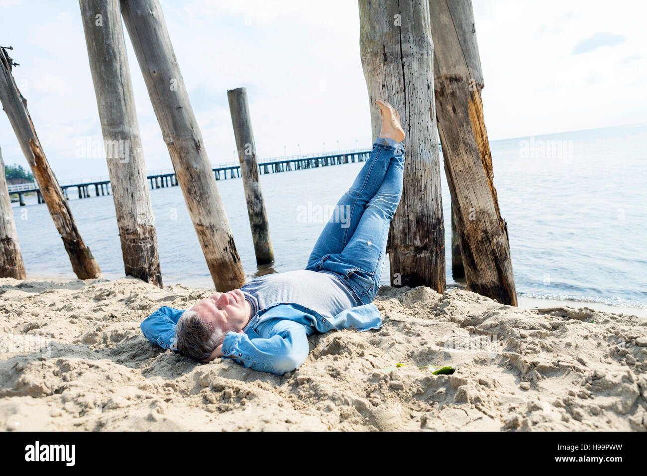 Uomo che stabilisce sulla spiaggia con i piedi fino Foto Stock