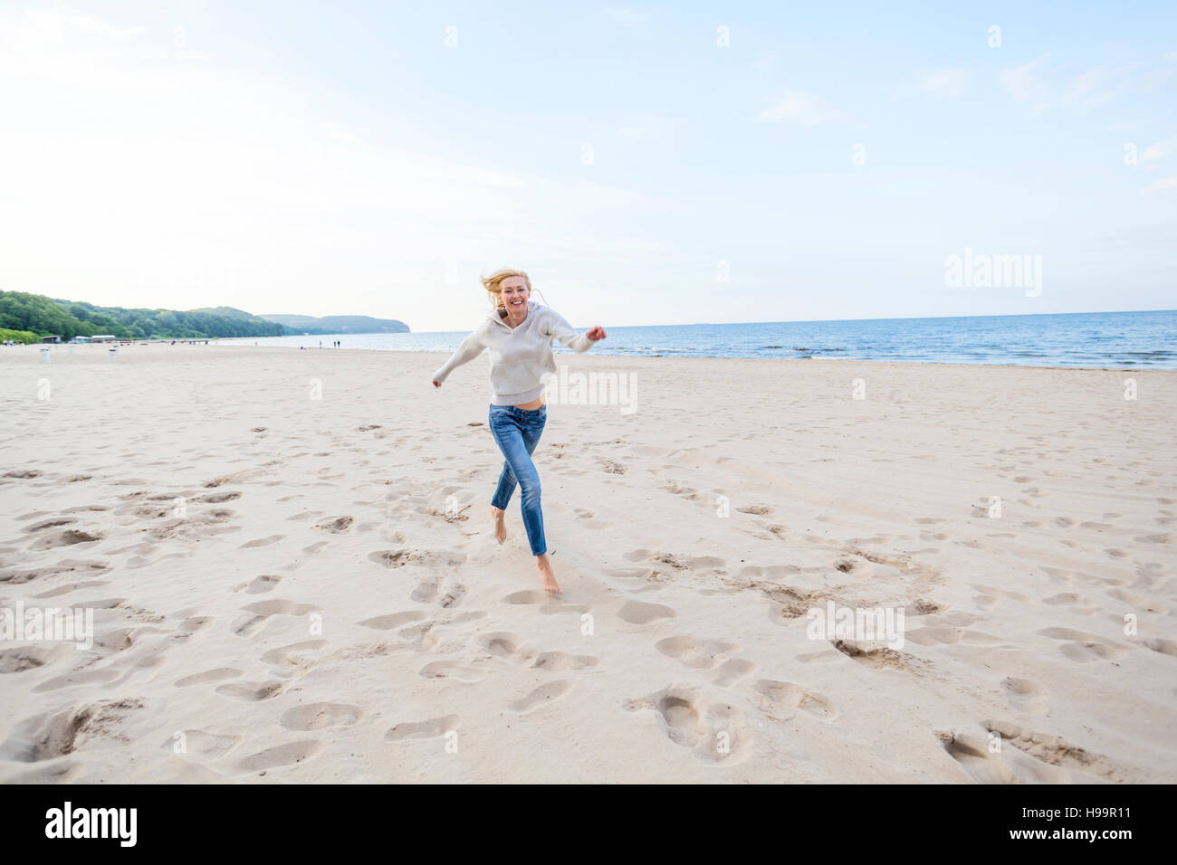 Donna con capelli biondi che corre lungo la spiaggia Foto Stock