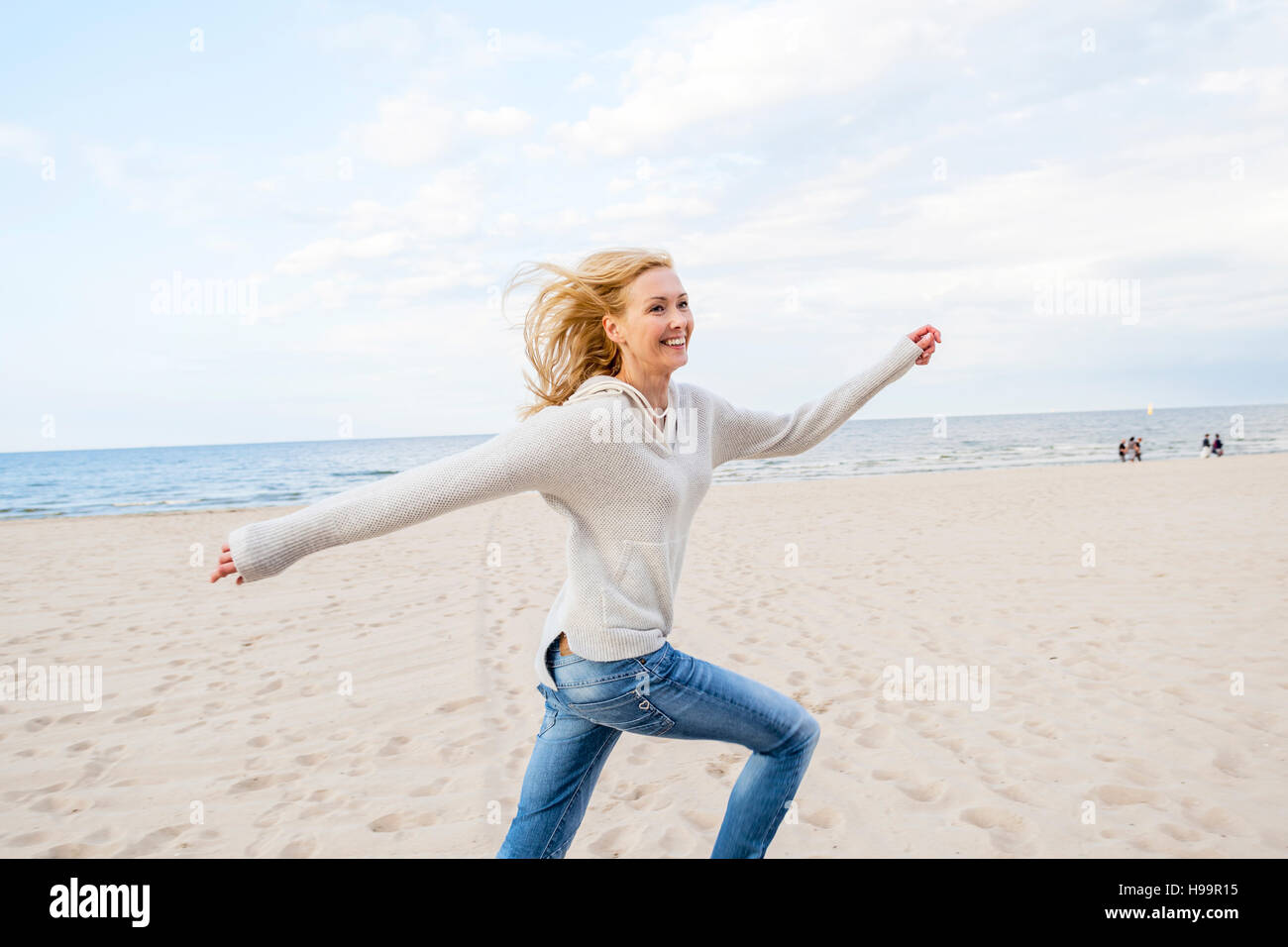 Donna con capelli biondi che corre lungo la spiaggia Foto Stock