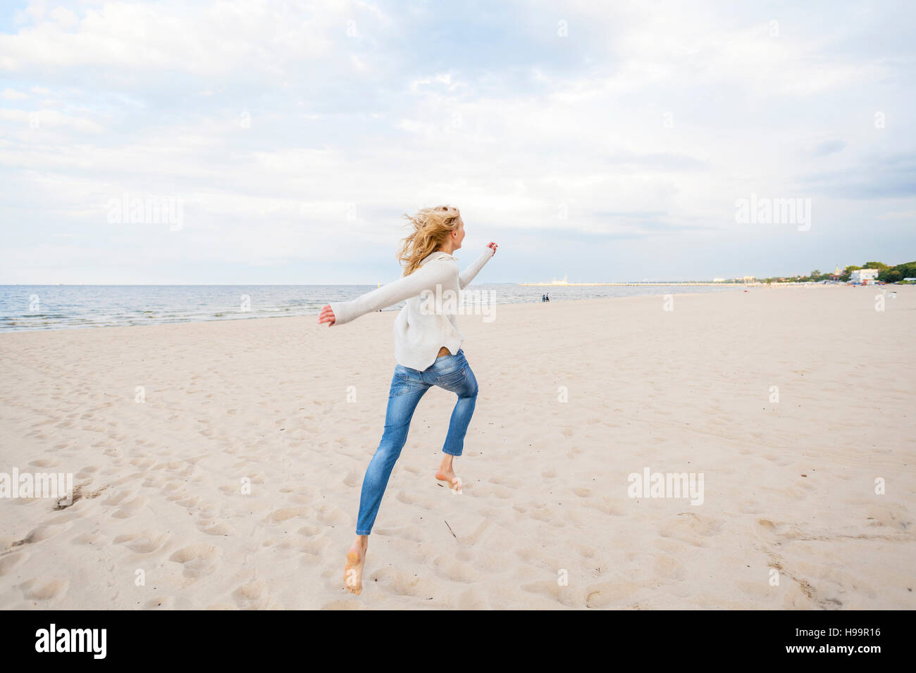 Donna con capelli biondi che corre lungo la spiaggia Foto Stock