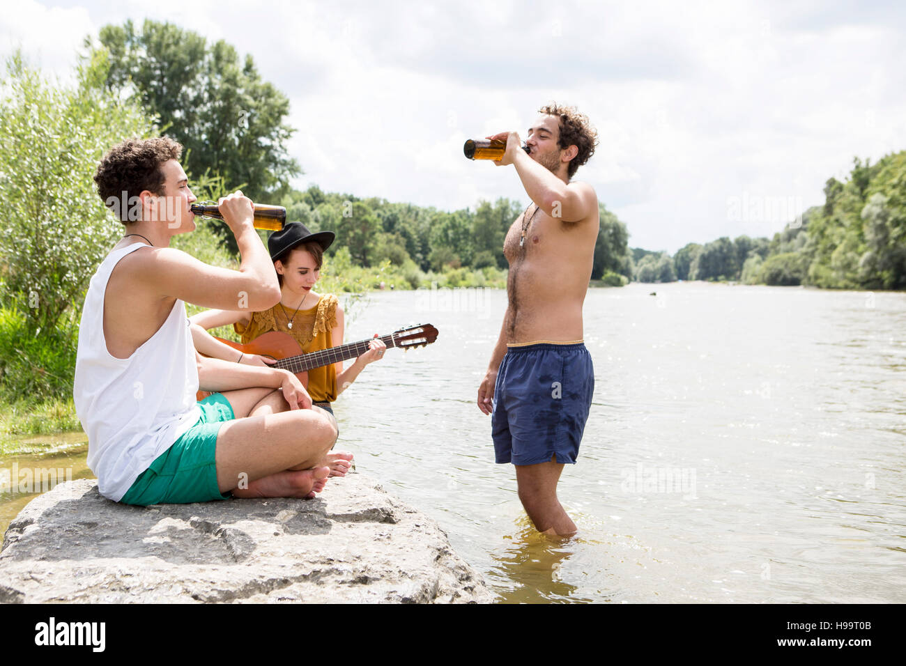 Gruppo di amici a bere birra sul greto del fiume Foto Stock