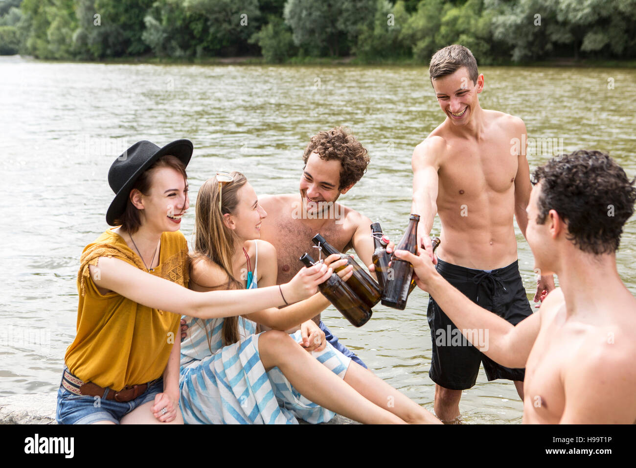 Gruppo di amici a bere birra sul greto del fiume Foto Stock