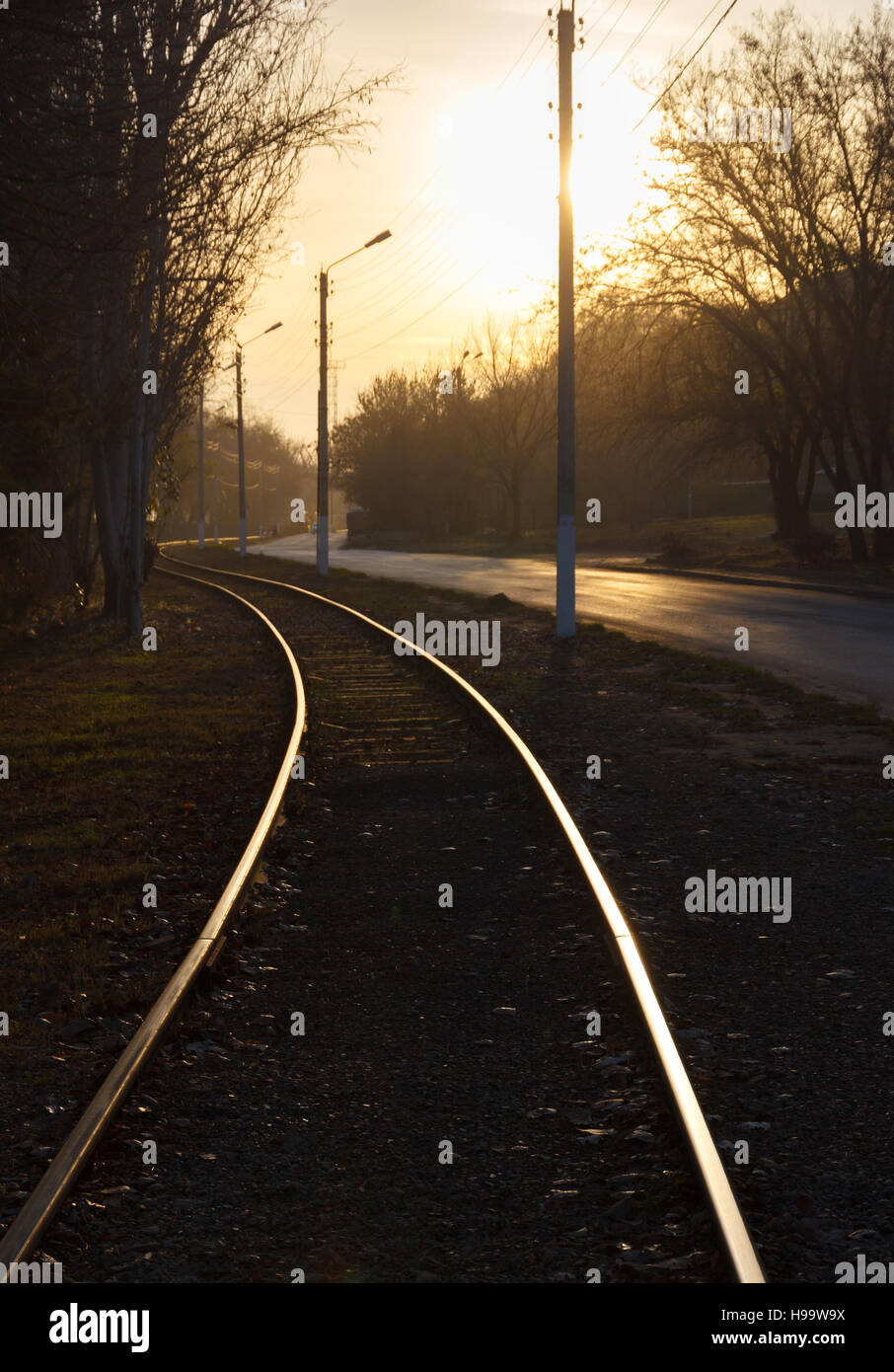 Binario ferroviario che corre lungo una strada al tramonto Foto Stock