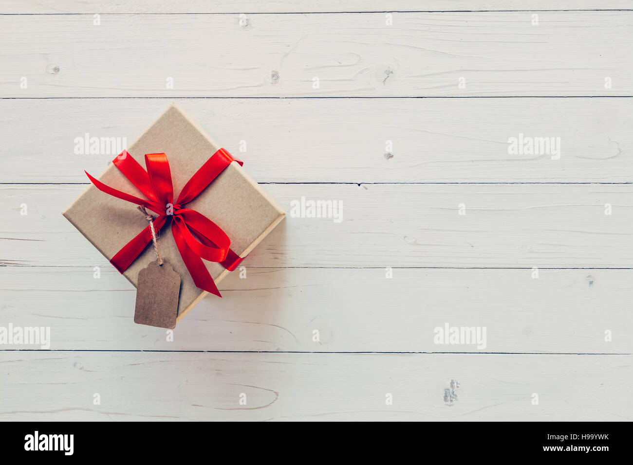 Brown box regalo con tag su sfondo di legno. Vintage scatola regalo su sfondo di legno. Confezione regalo con nastro rosso su uno sfondo di legno con lo spazio. Foto Stock