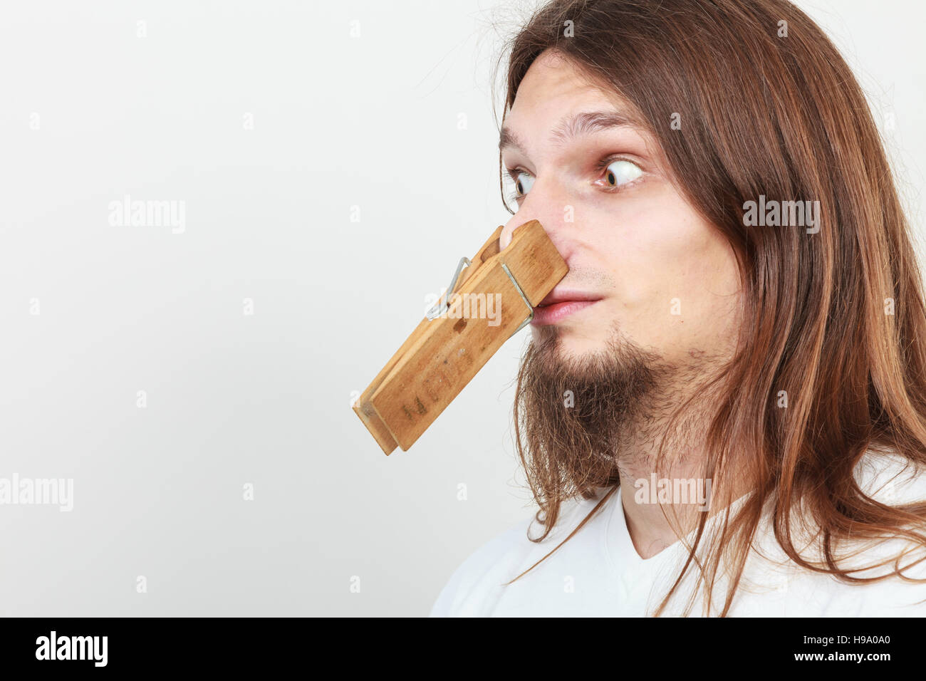 Uomo con clip clothespin peg sul suo naso. Giovani dai capelli lunghi guy sensazione sgradevole odore puzzano. Cattivo odore del concetto. Foto Stock