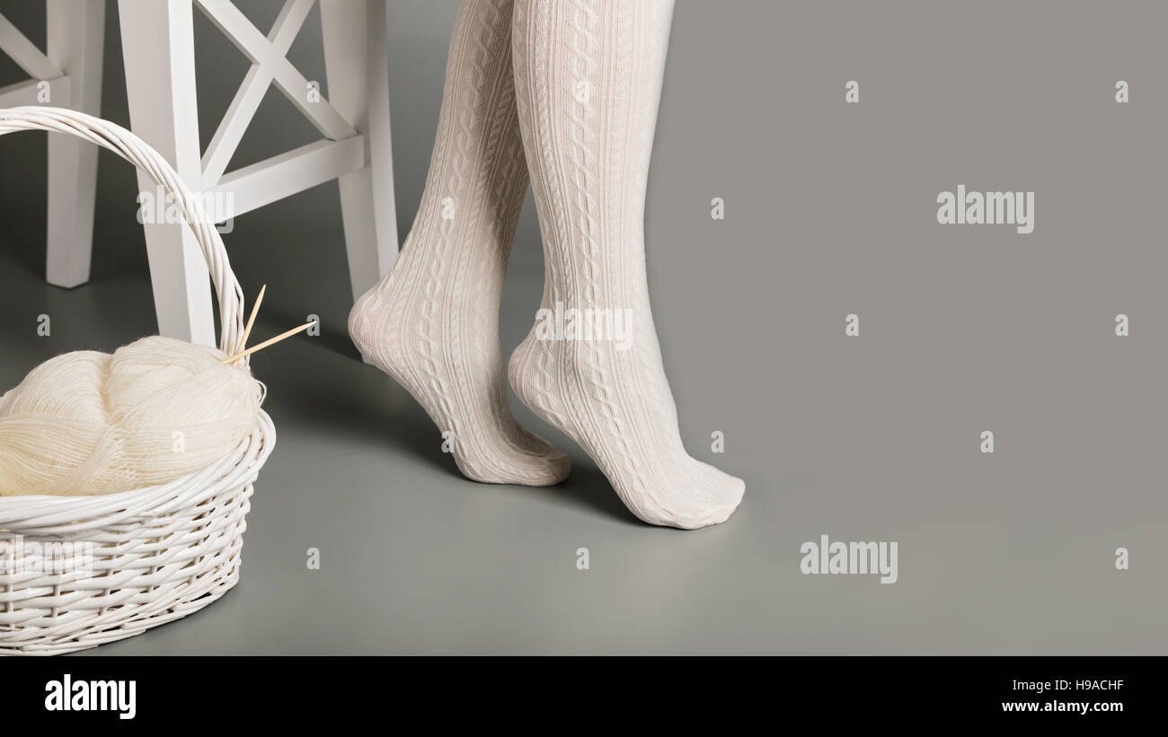 I piedi femminili in maglia bianco Collant in prossimità del cesto con filati e maglieria. Foto Stock