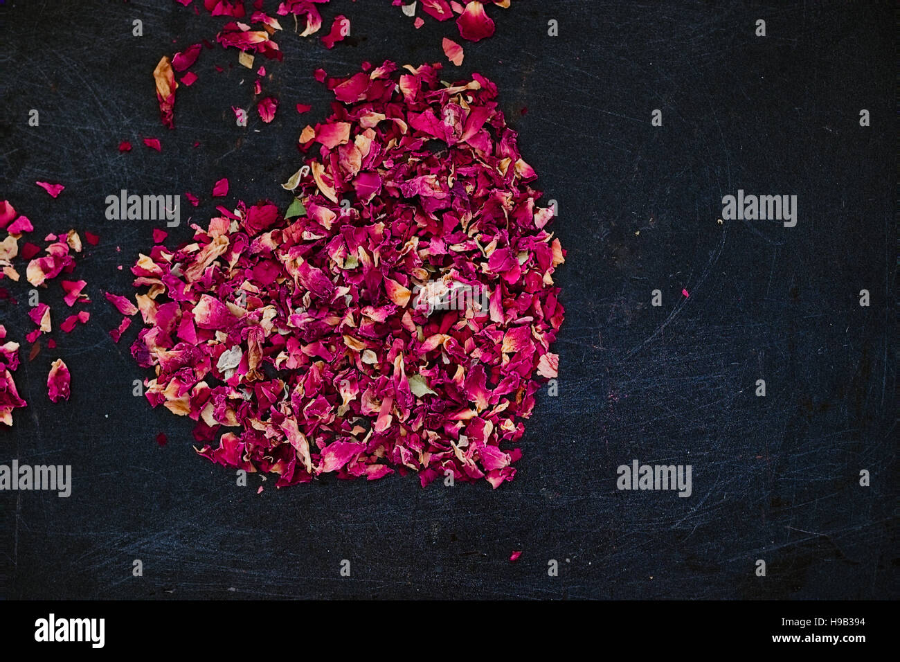 Essiccati petali di rosa a forma di cuore su uno sfondo scuro. Ingrediente romantico per il tè, vasca da bagno o cosmetici. Copia dello spazio. Copia dello spazio. Dark cibo fotografia Foto Stock