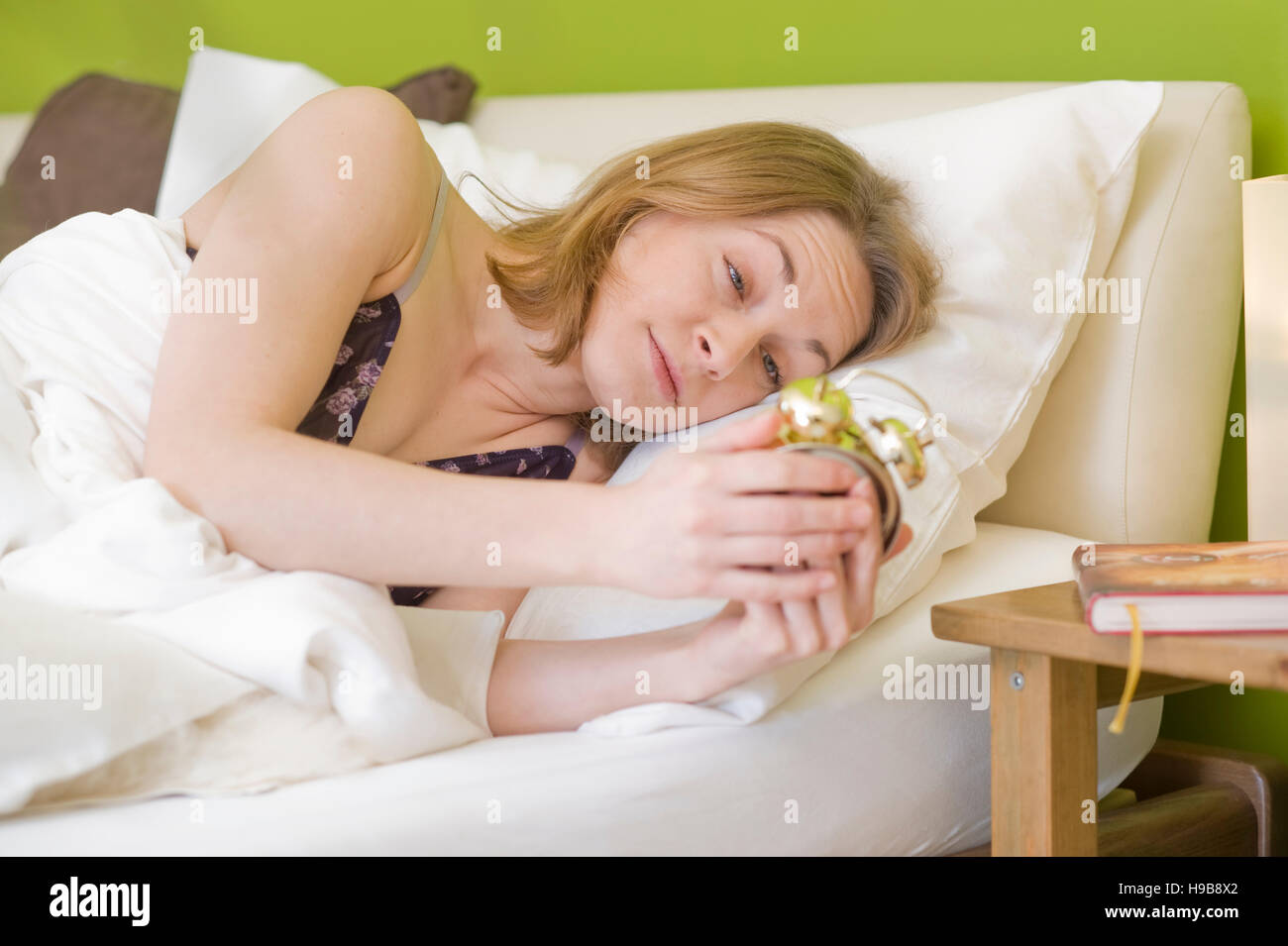 Stanco donna svegliarsi, guardando il suo orologio sveglia Foto Stock