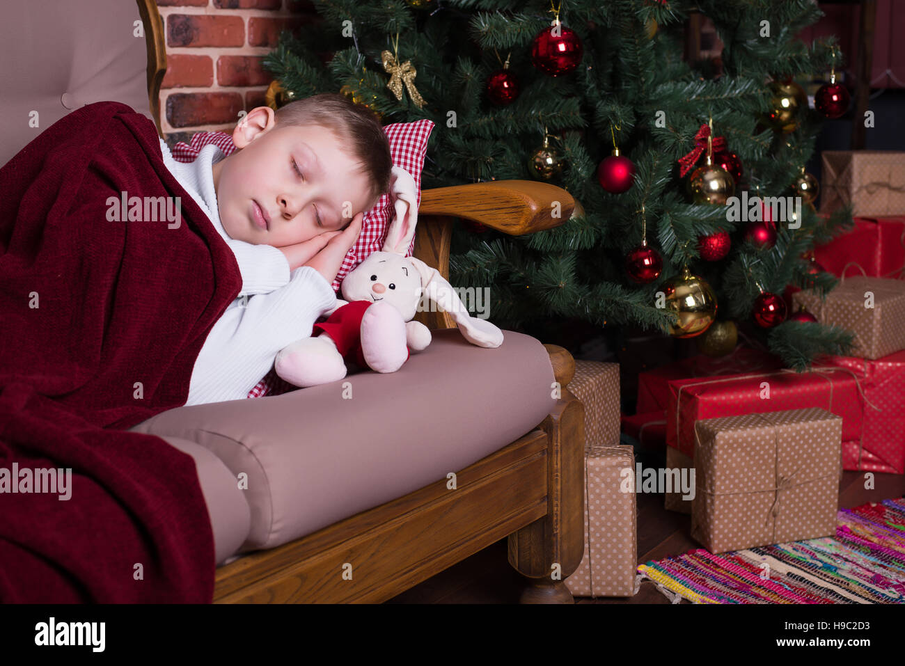 Ragazzo dormiva sotto una coperta sul divano vicino all'albero di Natale con doni Foto Stock