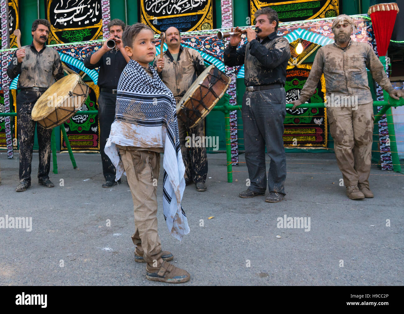 Sciita iraniano bambino musulmano con macchie di fango sui suoi vestiti di fronte musicisti durante il giorno di ashura, Lorestan provincia, Khorramabad, Iran Foto Stock