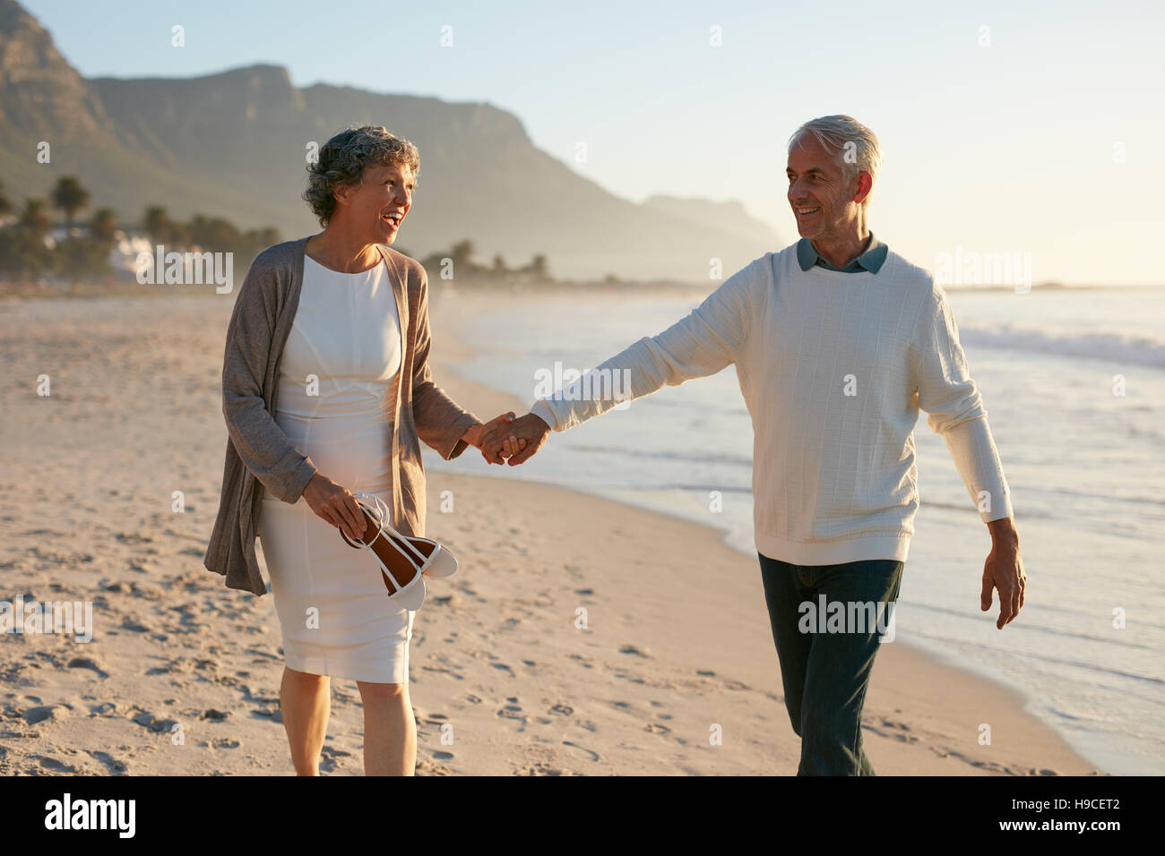 Colpo di amorevole coppia matura per passeggiare sulla spiaggia. Senior uomo e donna senior tenendo le mani e facendo una passeggiata sulla riva del mare. Foto Stock