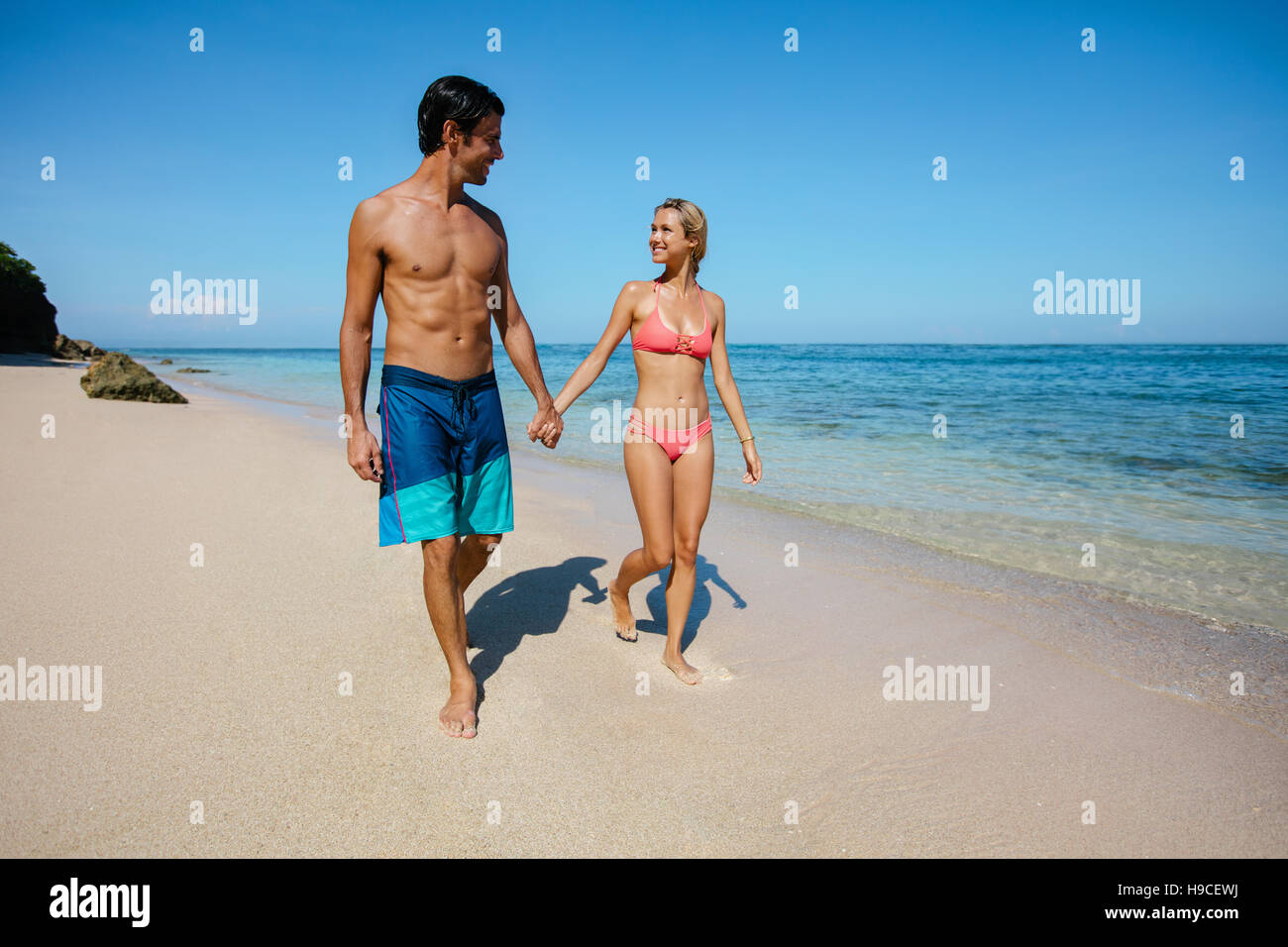 A piena lunghezza shot di coppia giovane tenendo le mani di camminare sulla spiaggia. Giovane uomo e donna per passeggiare sulla riva del mare. Foto Stock