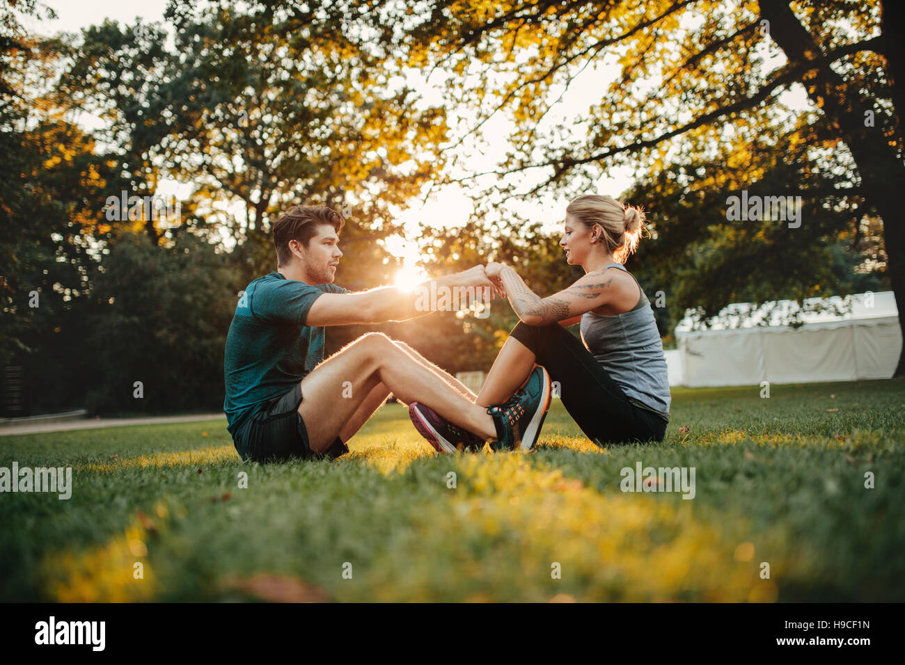 Coppia giovane cooperante durante lo stiramento al parco. L uomo e la donna seduta insieme tenendo le mani e di esercizio. Foto Stock