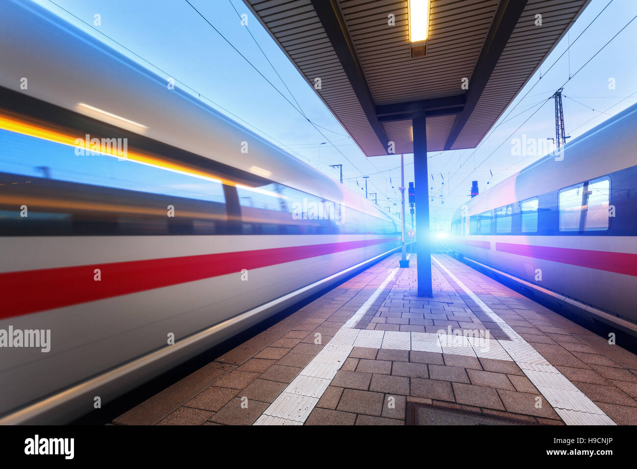 Alta velocità treni passeggeri sulla piattaforma ferroviario in movimento al crepuscolo. Treno sfocata. Stazione ferroviaria di notte con la luce in Europa Foto Stock