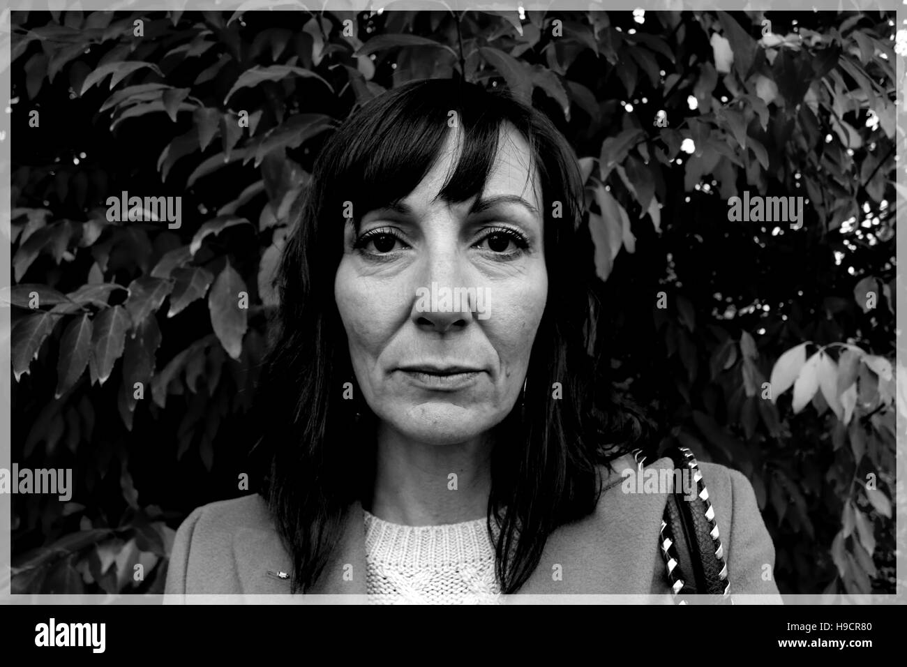 Chiudere fino in bianco e nero ritratto di donna con un triste e moody espressione nella parte anteriore delle foglie Foto Stock Chiudere fino in bianco e nero ritratto di donna con un triste e moody espressione nella parte anteriore delle foglie Foto Stock