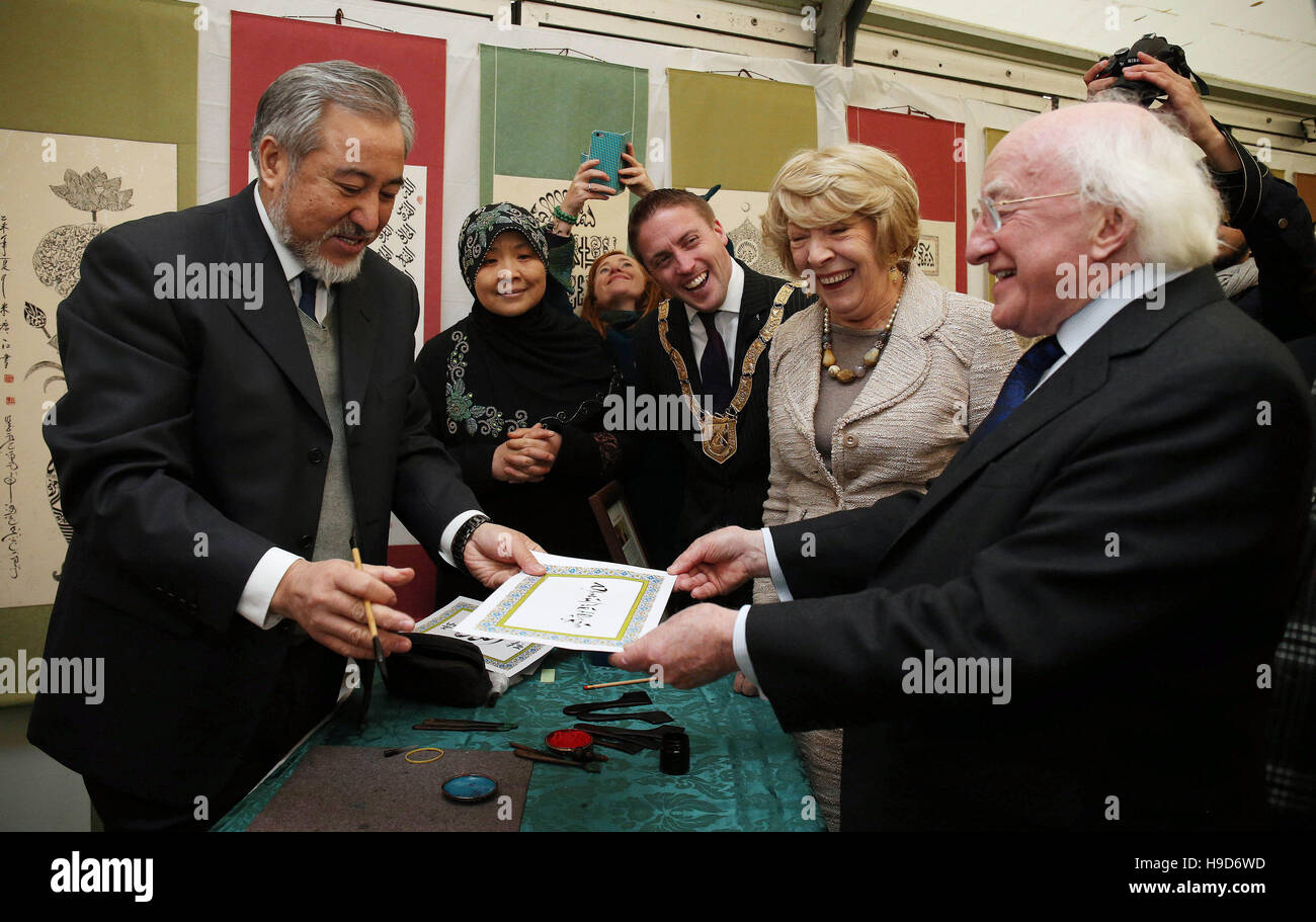 Presidente irlandese Michael D Higgins (destra) presenta maestro calligrafo Haji Noor Deen Mi Guang Jiang (sinistra) con qualche lingua irlandese calligrafia, come il Presidente la moglie Sabina Coyne (seconda a destra) e Cormac Devlin, Cathaoirleach di Dun Laoghaire Rathdown County Council a guardare, durante una visita al Centro Culturale Islamico di Irlanda, Clonskeagh, Dublino il suo ventesimo anniversario. Foto Stock