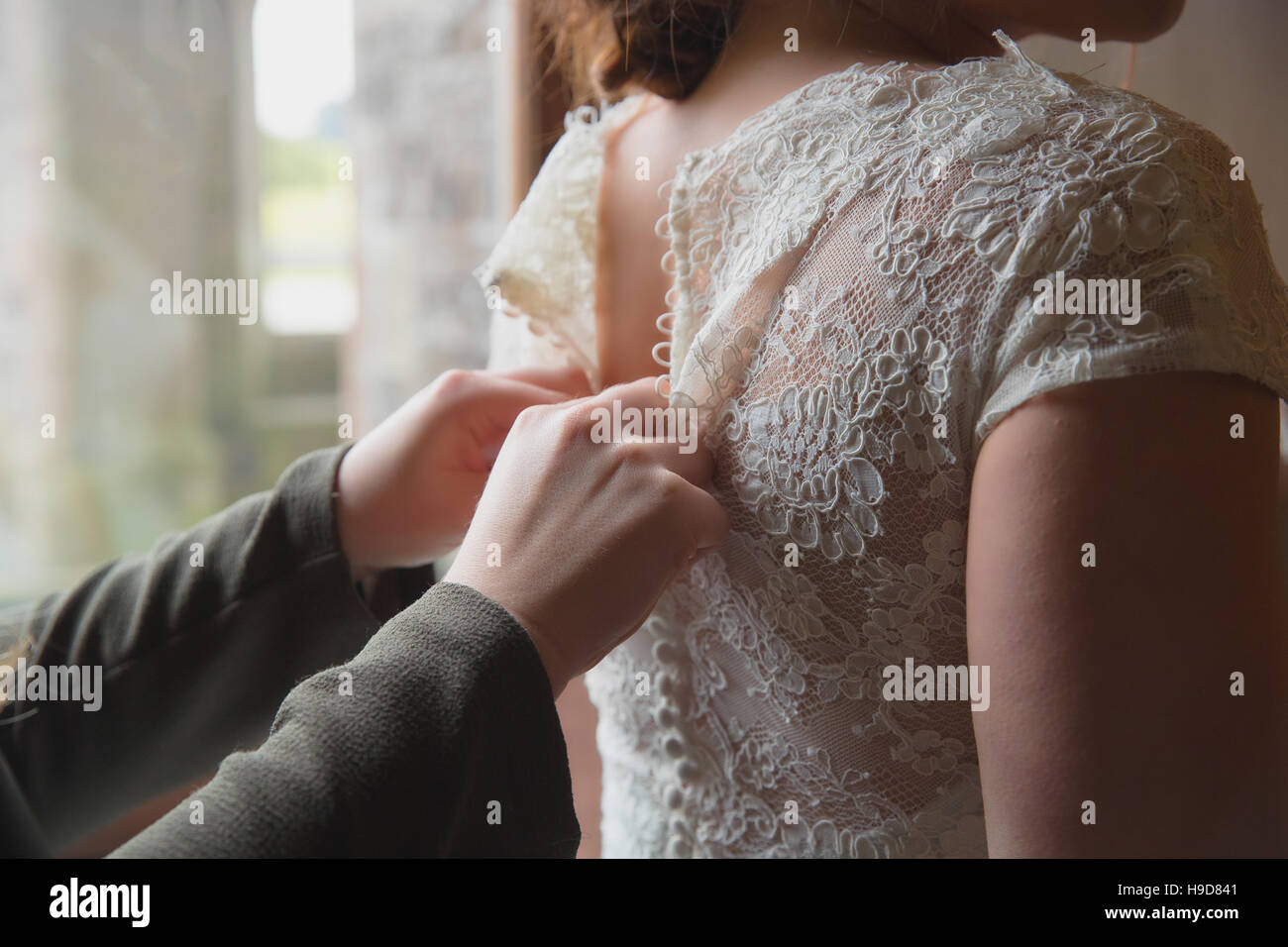 Con cura le mani facendo fino i pulsanti su un abito da sposa Foto Stock