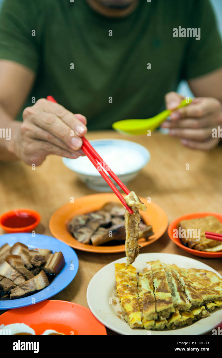 Un uomo mangia Uova salate, brasati e frittata con congee Tai Buan Porridge, una mensa cinesi in Penang specializzato in riso congee e brasati. Foto Stock