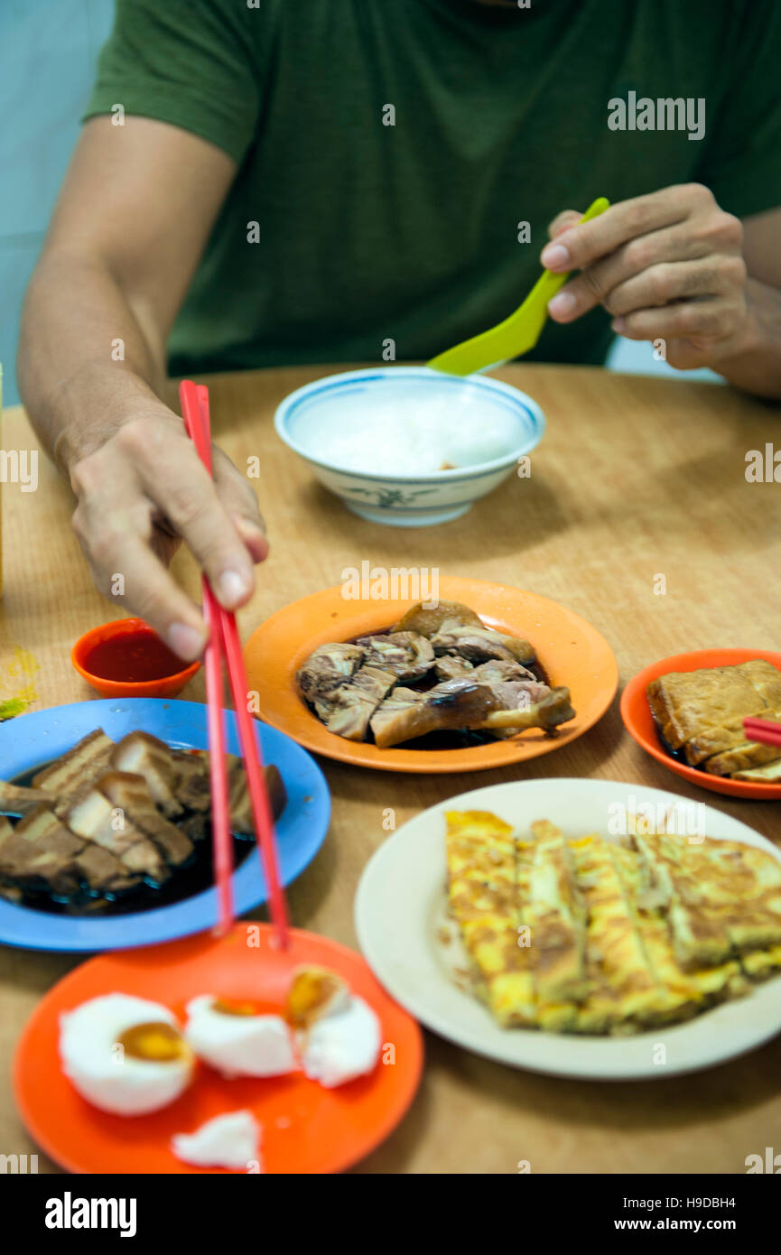 Un uomo mangia Uova salate, brasati e frittata con congee Tai Buan Porridge, una mensa cinesi in Penang specializzato in riso congee e brasati. Foto Stock