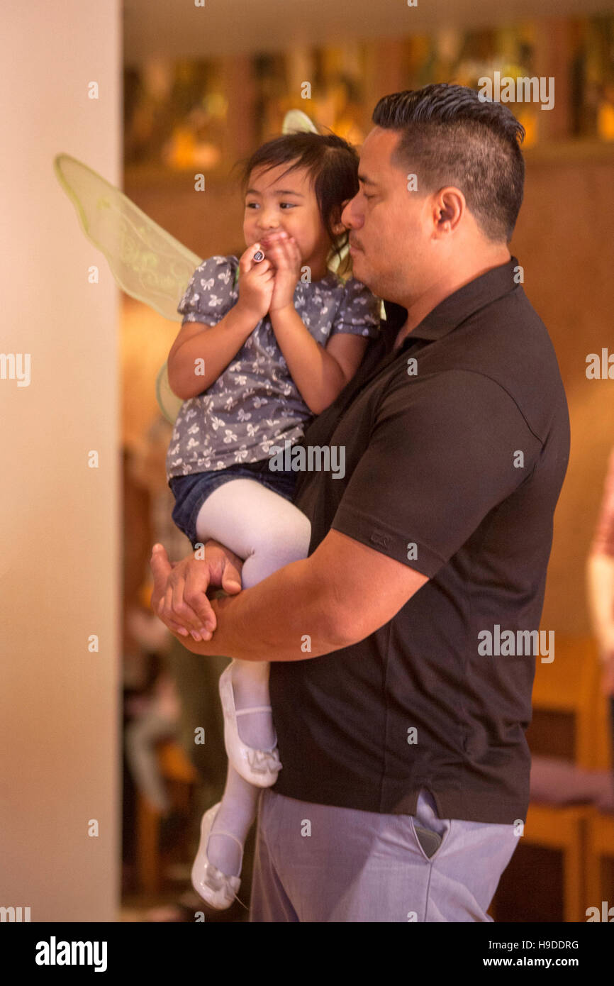 Una ragazza ispanica indossando ali d'angelo è detenuto da suo padre durante la messa in una Laguna Niguel, CA, chiesa cattolica. Foto Stock