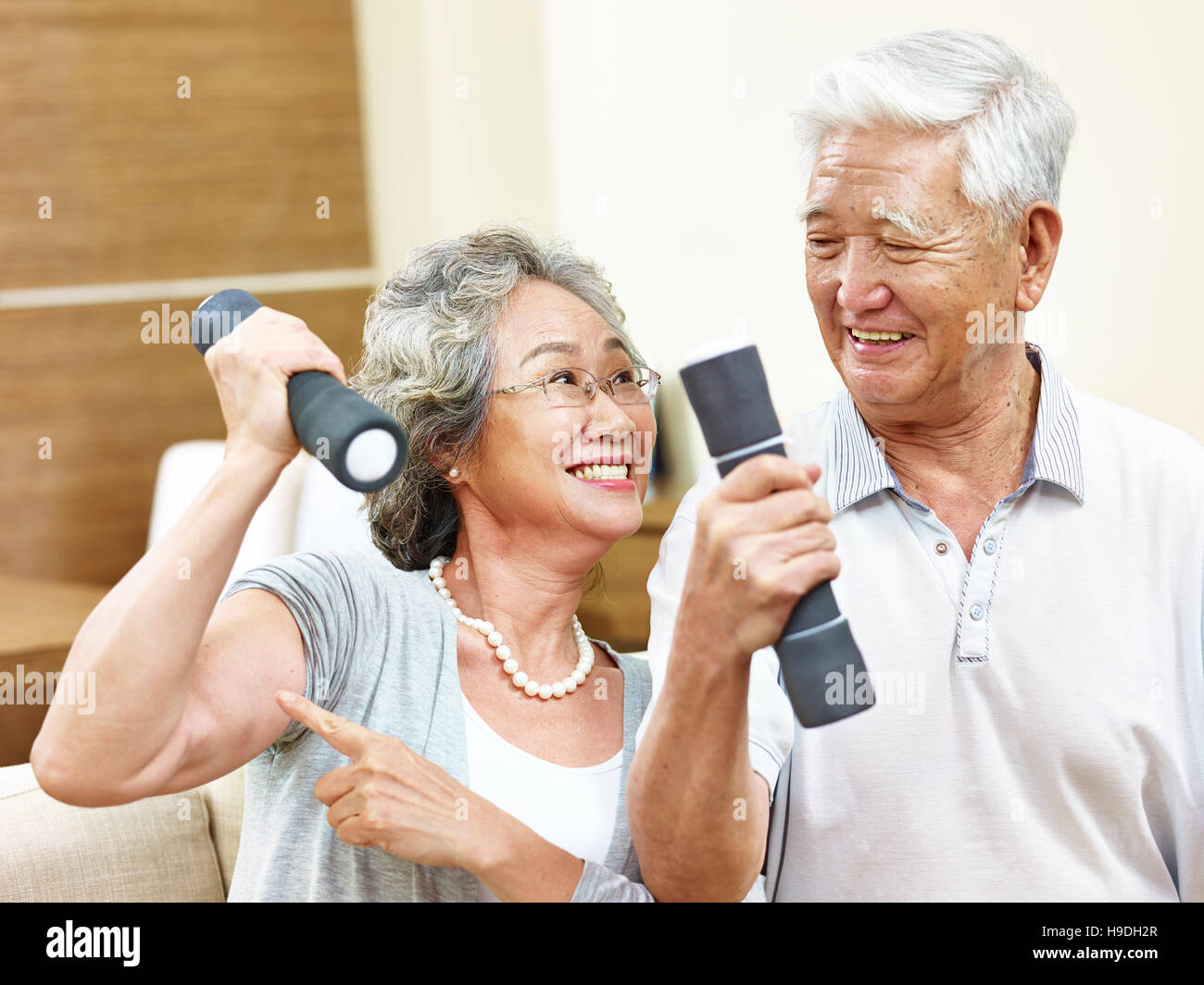 Felice senior donna asiatica holding dumbbell mostrando il suo muscolo per marito Foto Stock