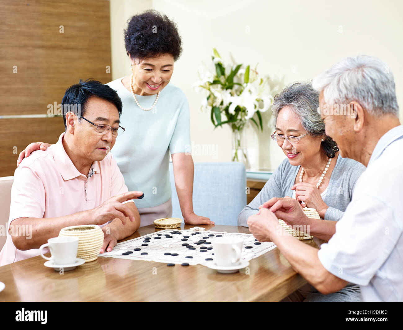 Due alti uomini giocando Weiqi (o gioco del go) a casa con le loro mogli guardando Foto Stock